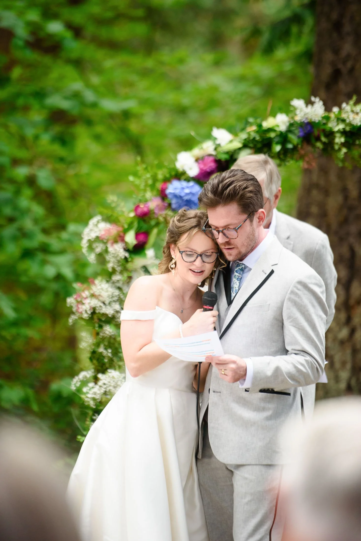 Wedding photo at Hoyt Arboretum of A bride and groom reading wedding vows during an outdoor wedding ceremony, with a floral arch and greenery in the background.