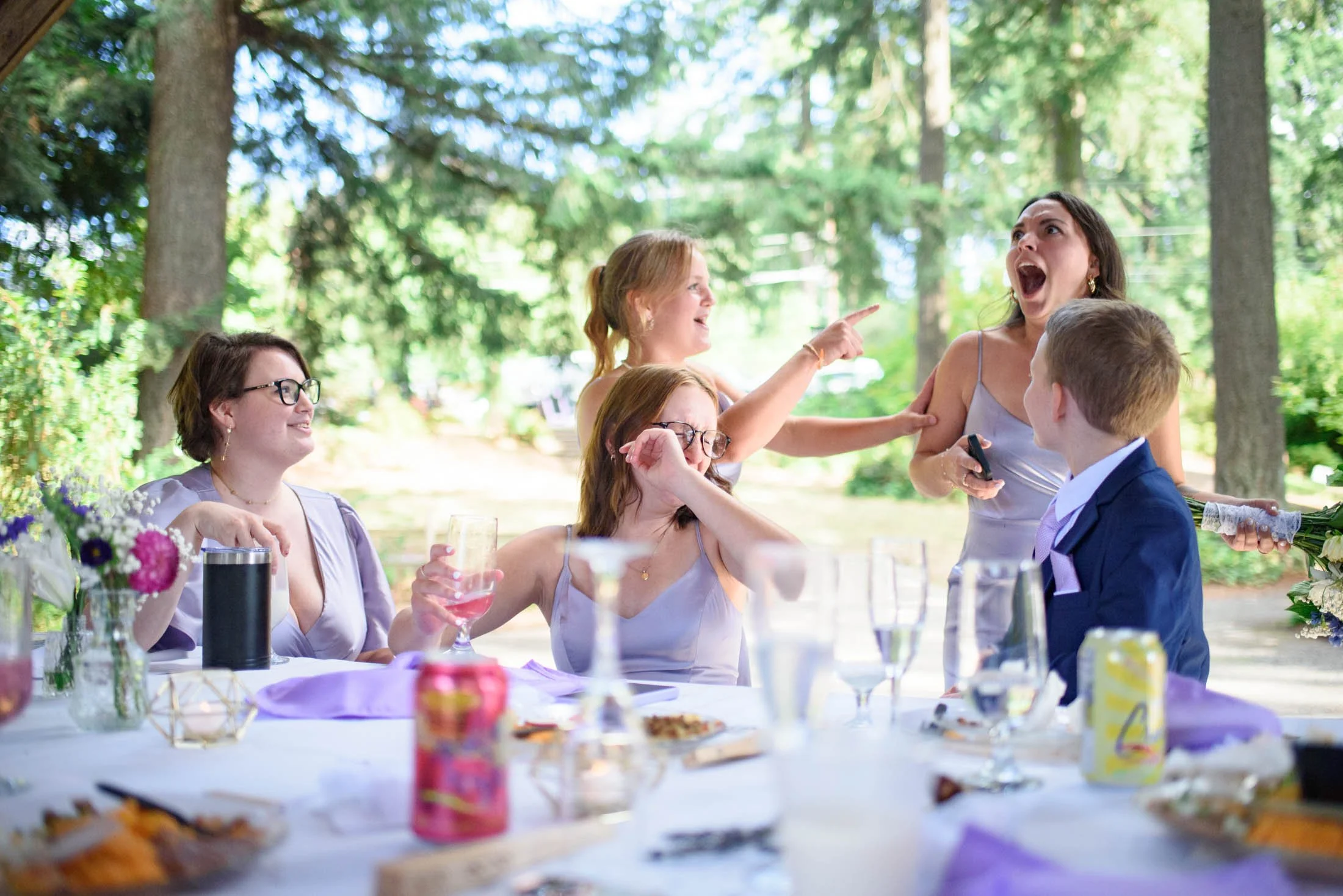 Wedding photograph at Portland's Hoyt Arboretum of Group of women and a young boy at an outdoor celebration table, with trees in the background, engaged in conversation and laughter.