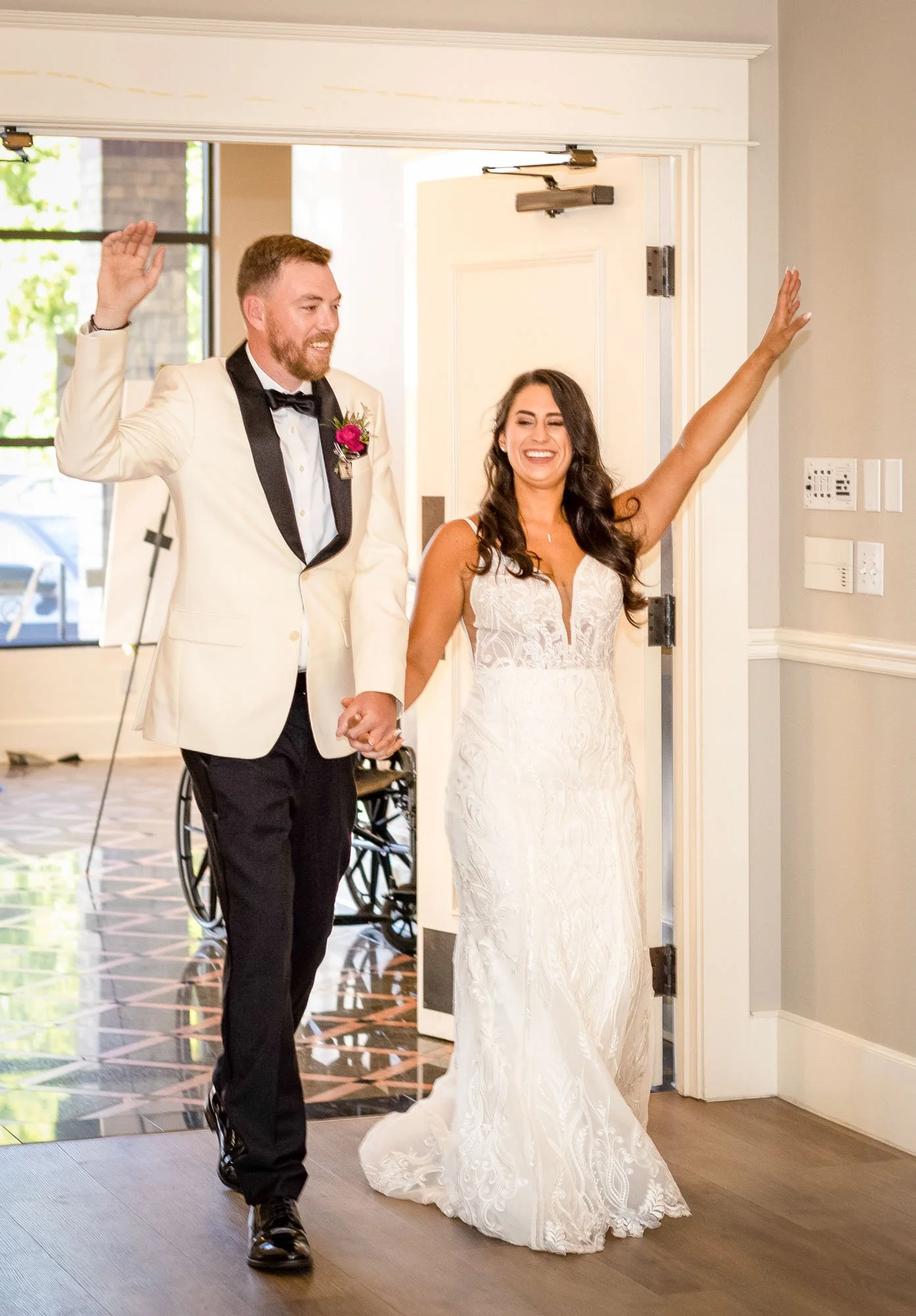 Happy bride and groom holding hands, walking into a room, smiling and waving, after wedding ceremony at Abernethy Center.