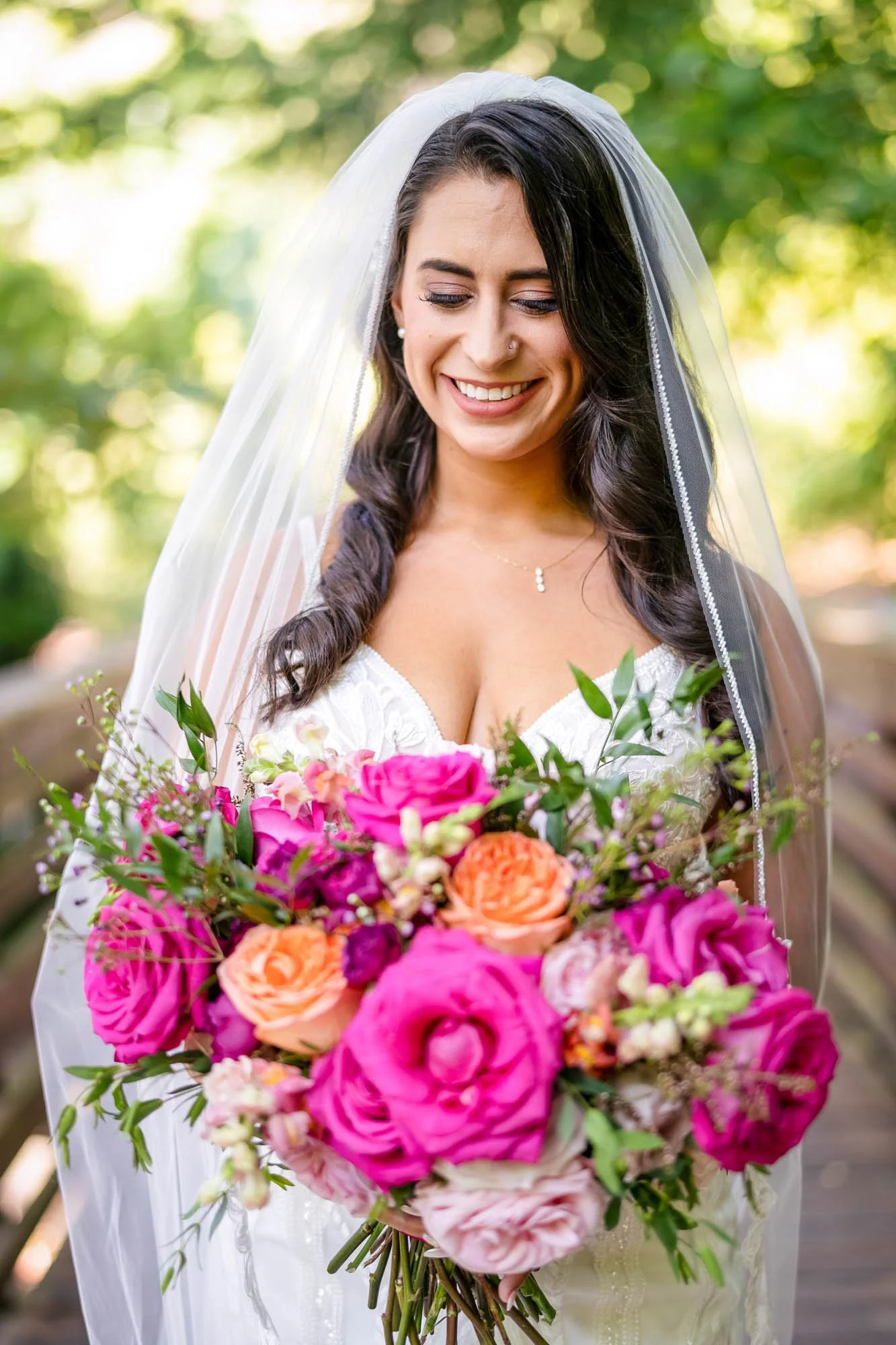 Wedding photo at Abernethy Center of a Bride holding a colorful bouquet of pink, orange, and purple flowers, smiling with eyes closed outdoors.
