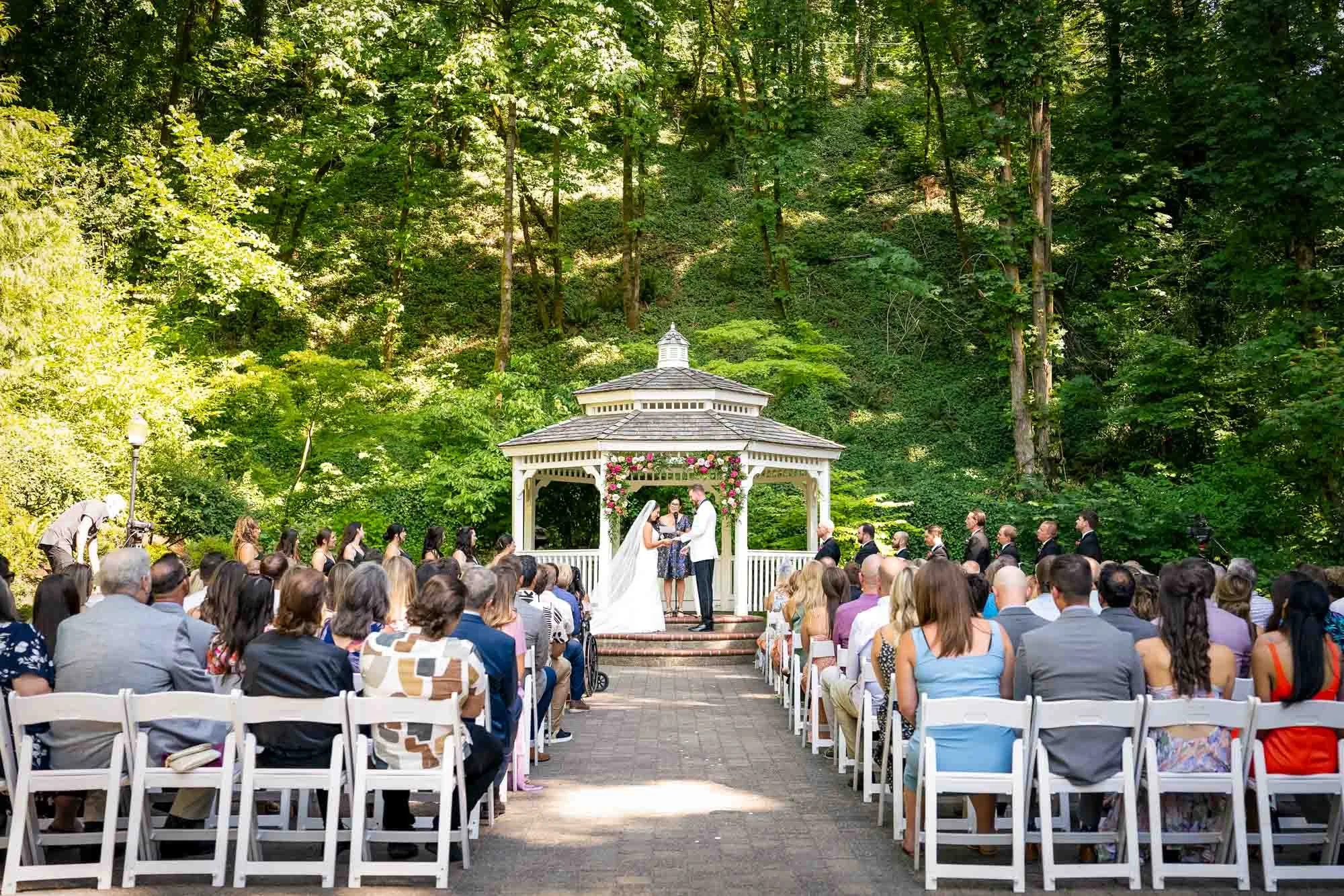 Abernethy Center and Gardens outdoor wedding ceremony taking place in a wooded area with a gazebo decorated with pink flowers called Abigail's Garden.