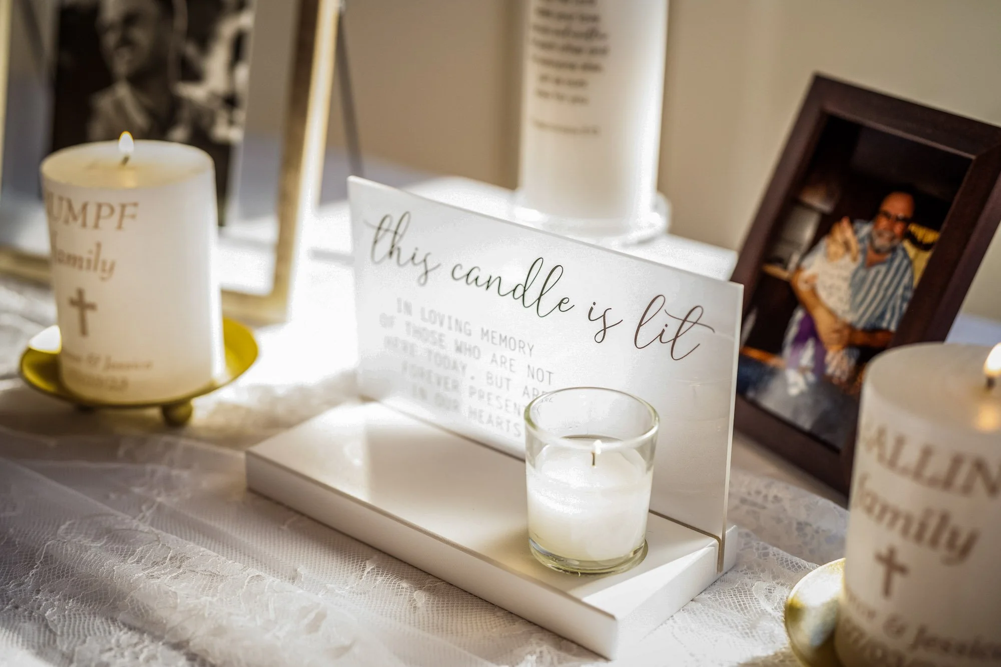 Wedding photo at Abernethy Center's Abernethy Chapel of A memorial table with lit candles, a framed photo of a man, and decorative signs, including a sign that says 'this candle is lit' and candles with religious messages.
