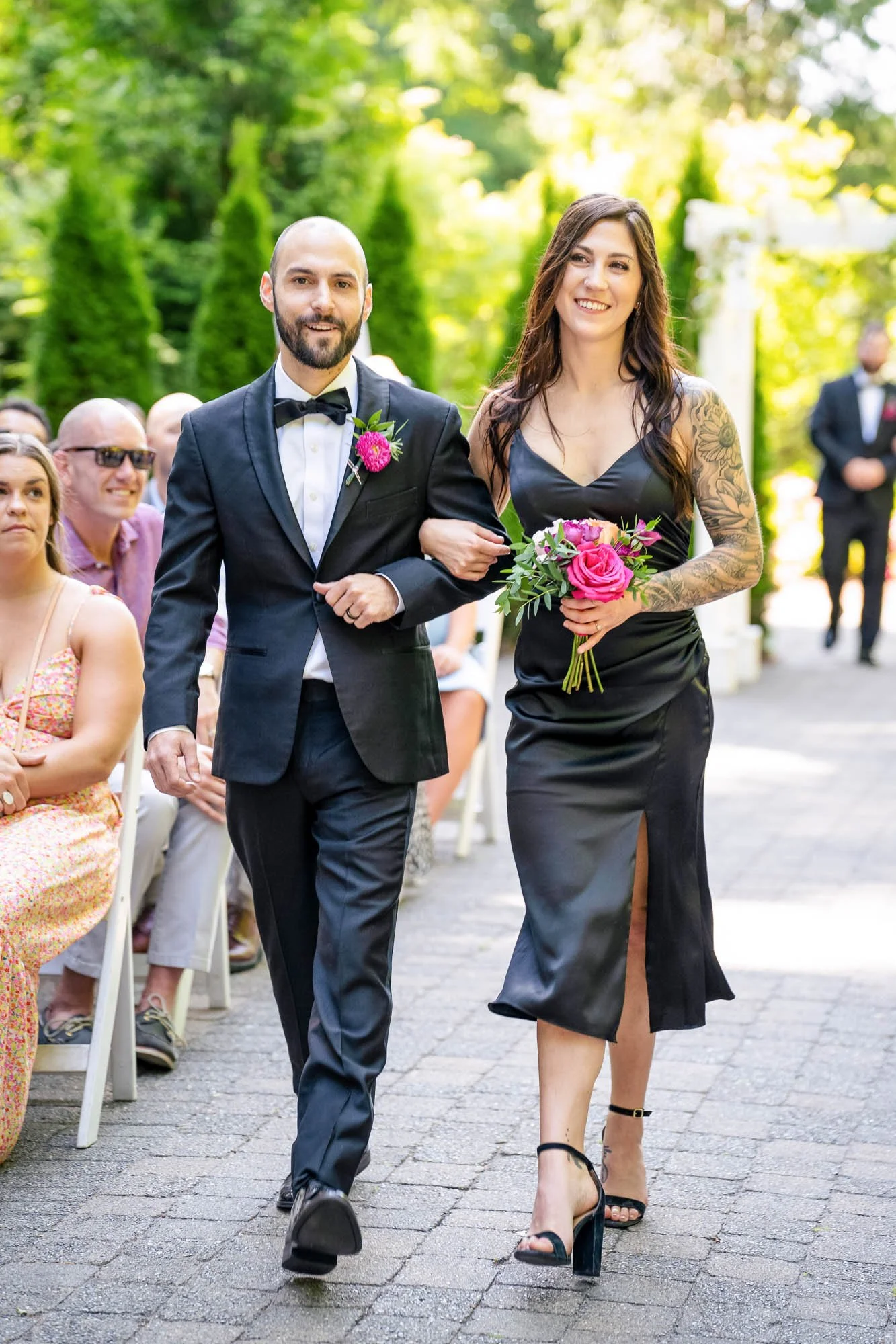 Wedding photography at Abernethy Center of A bride and groom walking down an outdoor aisle, holding hands, with wedding guests seated on either side, surrounded by greenery.