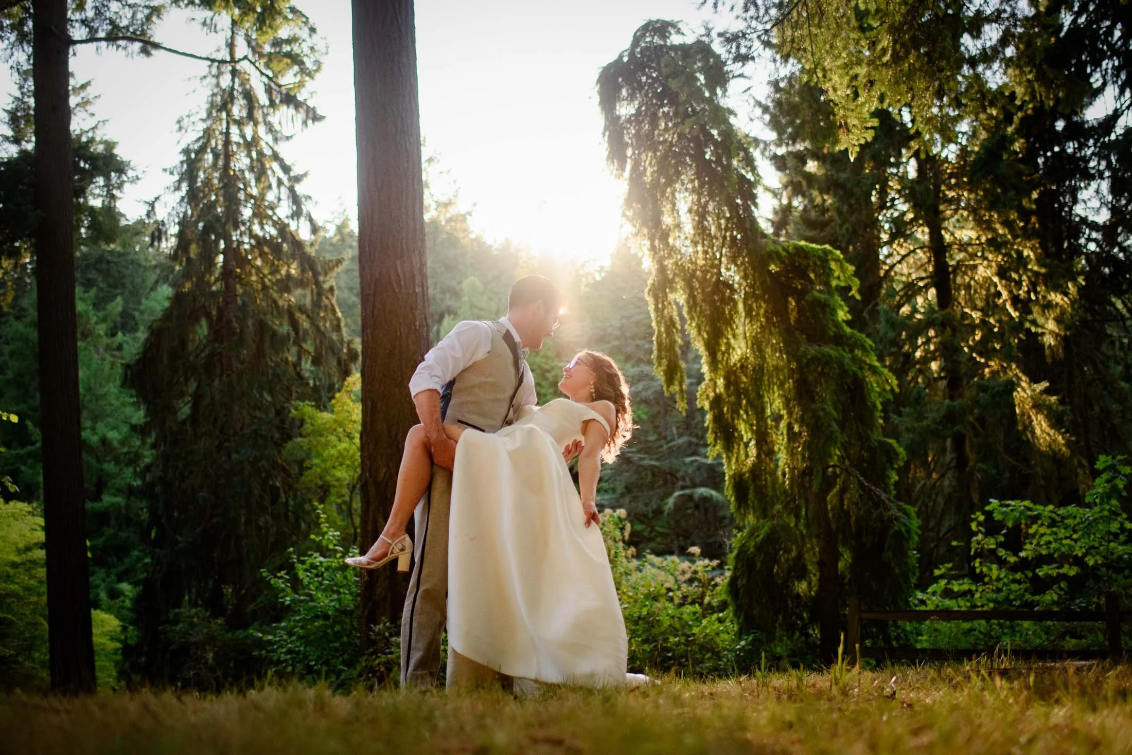 Wedding photograph at Portland's Hoyt Arboretum of A groom dips a bride in a forest during sunset on their wedding day, with tall trees and green foliage in the background.