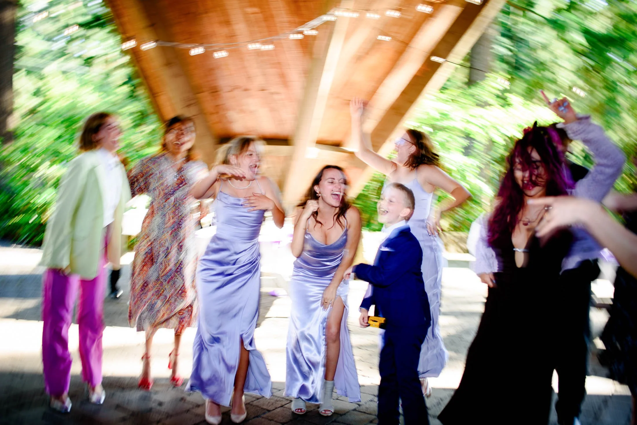 Wedding photograph at Portland's Hoyt Arboretum of A group of people laughing and dancing at a celebration or party with a wooden roof and green trees in the background.
