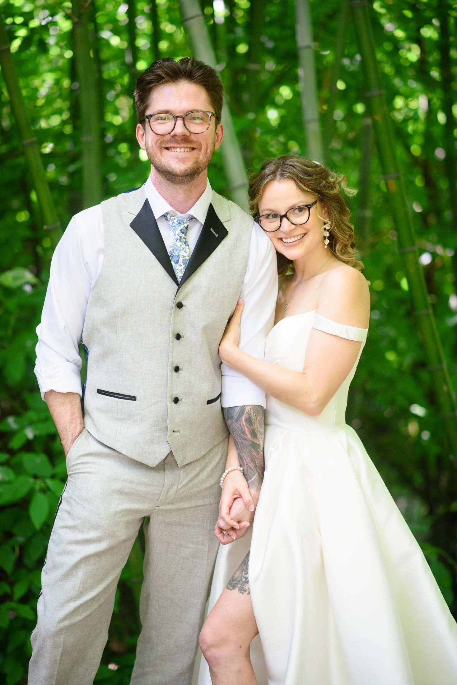 A happy couple in wedding attire standing outdoors in front of lush green foliage at Hoyt Arboretum in Portland wedding.