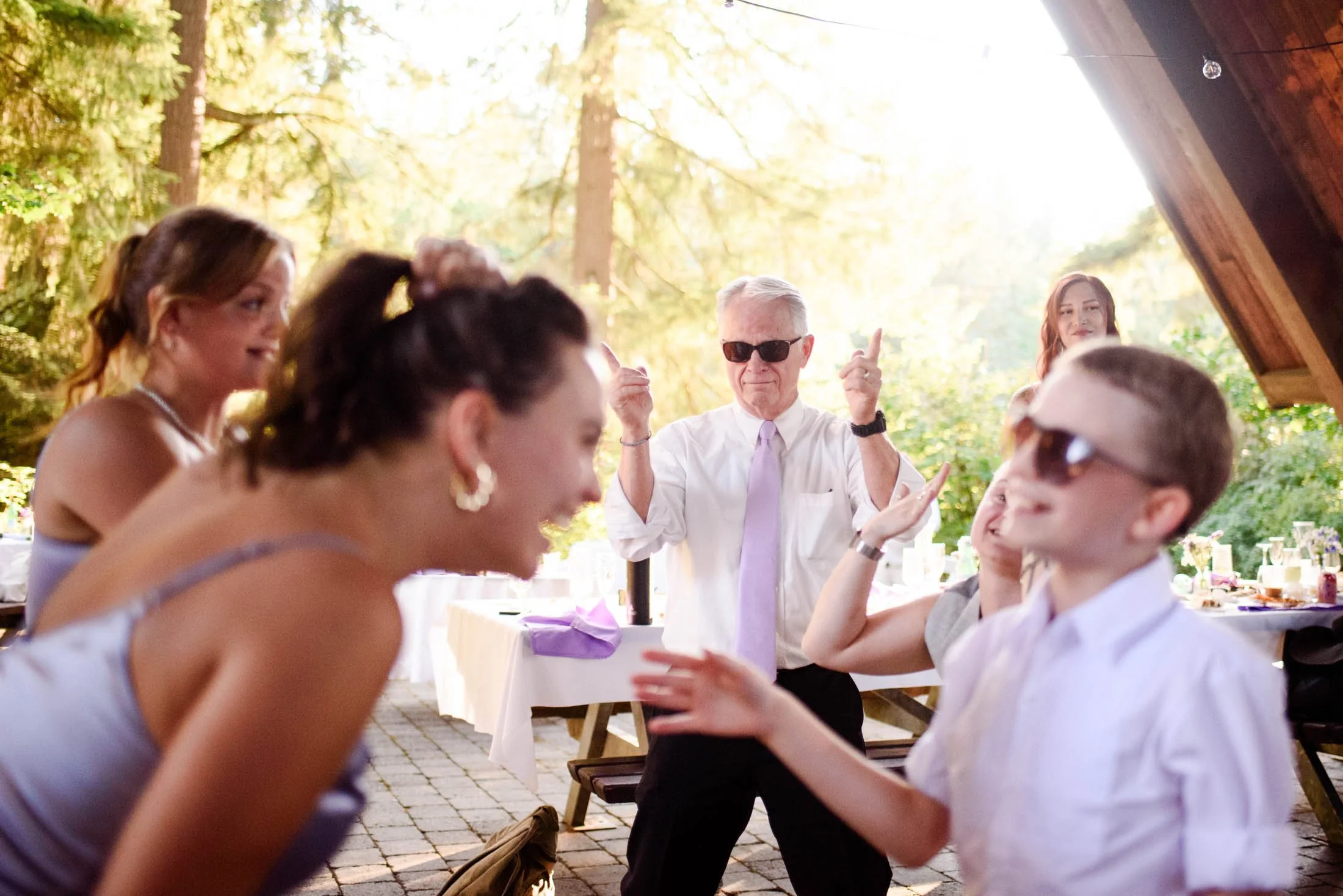 Wedding photograph at Portland's Hoyt Arboretum of A group of people dancing and enjoying at an outdoor event on a sunny day, with trees and picnic tables in the background.