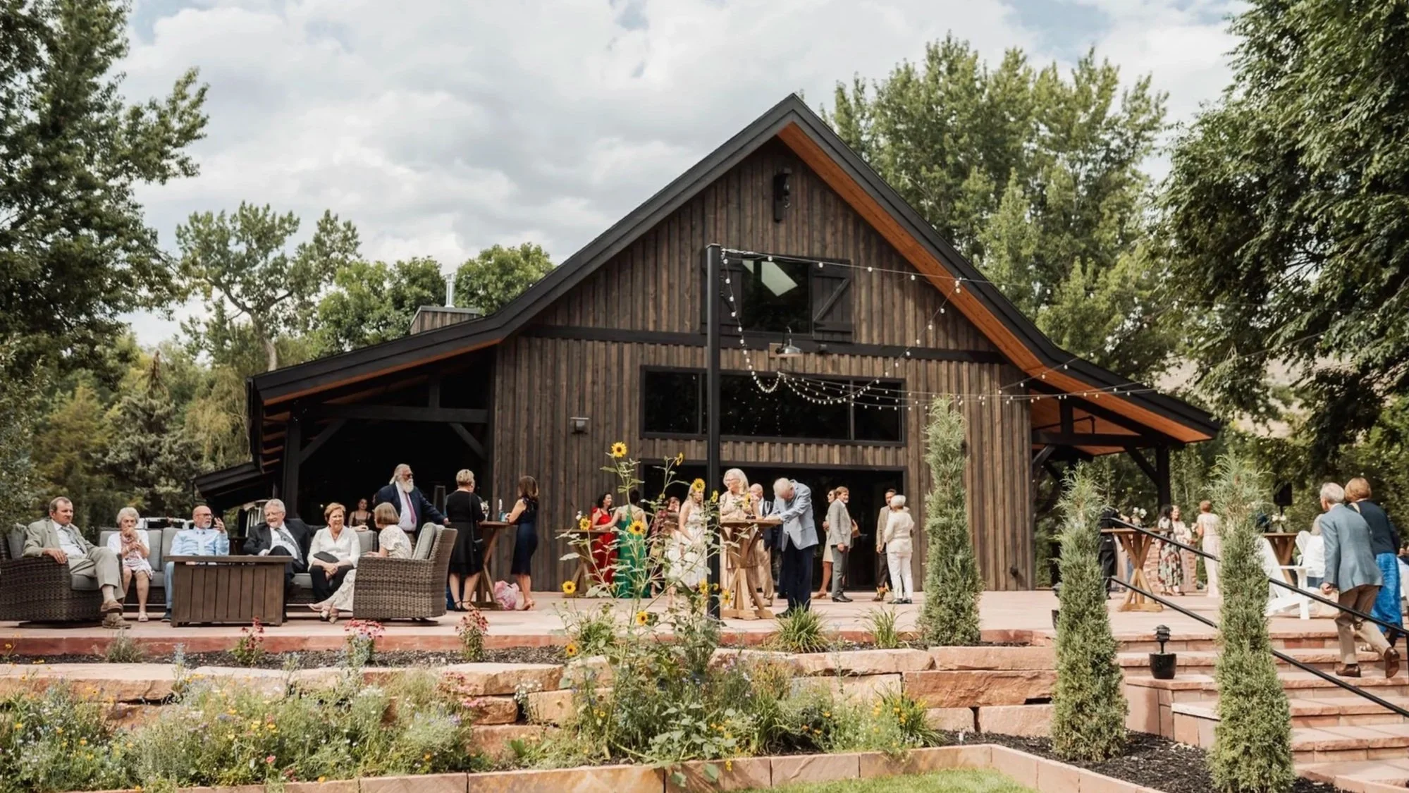 modern-barn-wedding-venue-with-guests-and-blue-sky-and-landscaping-with-flowers-in-bloom.jpg