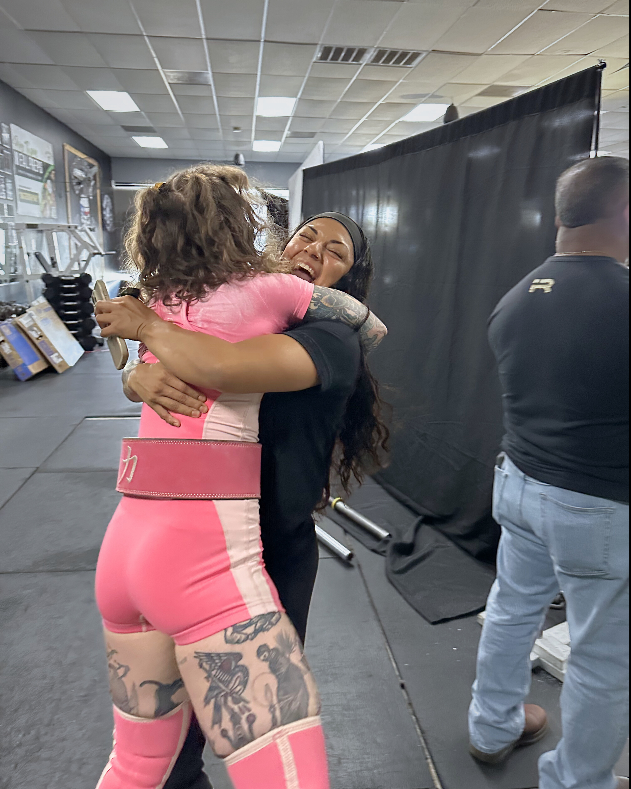 Two women hugging and smiling at each other in a gym or fitness center.