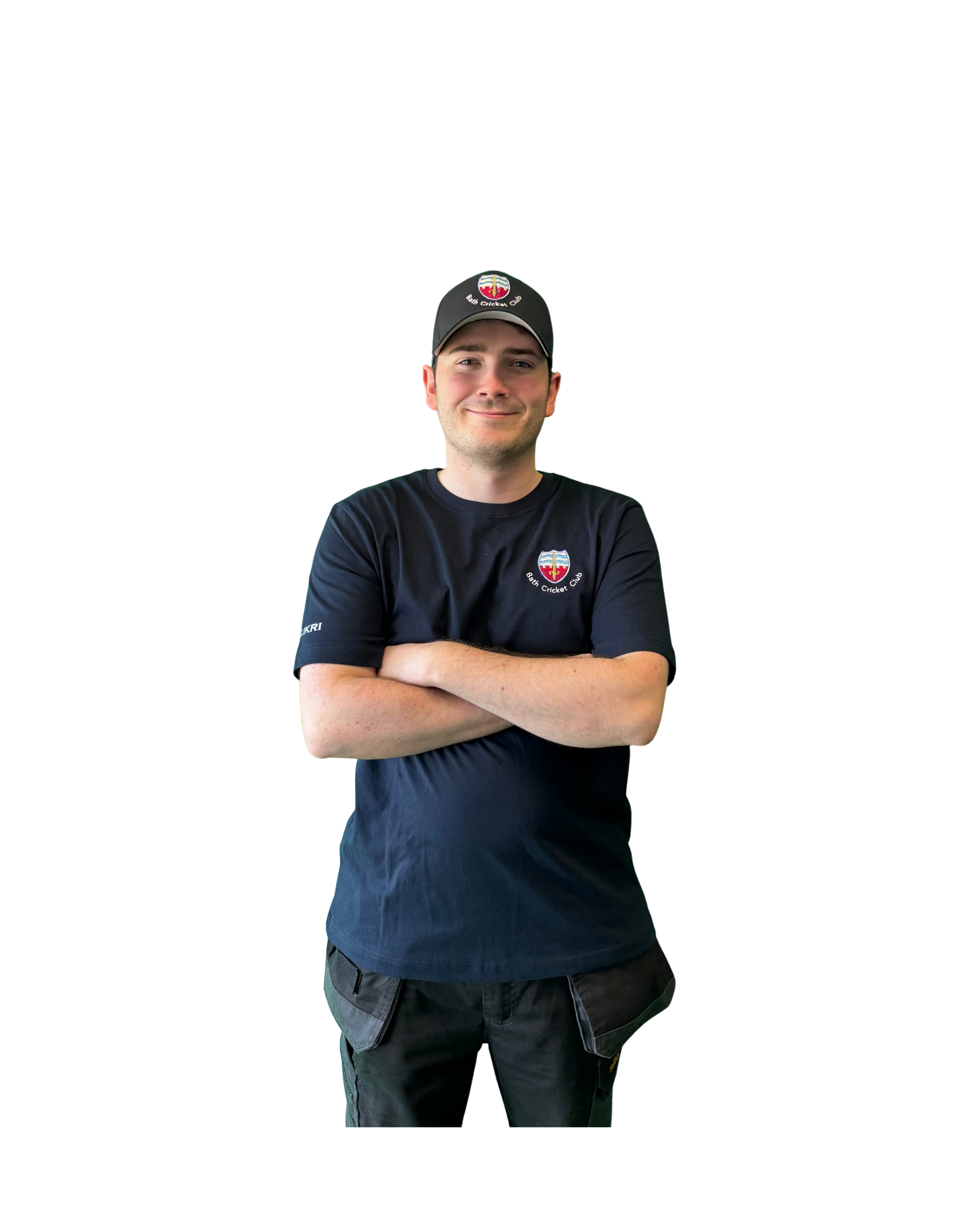A young man smiling with arms crossed, wearing a black baseball cap with a logo, and a black T-shirt with a crest emblem.