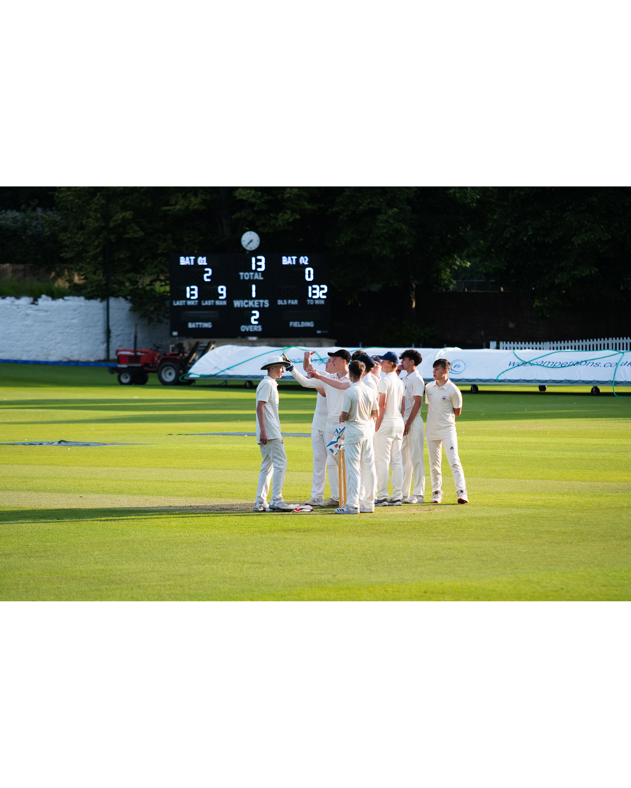 Cricket players on field celebrating, scoreboard in background showing 13 runs, 2 wickets, 132 runs to win, and match details.