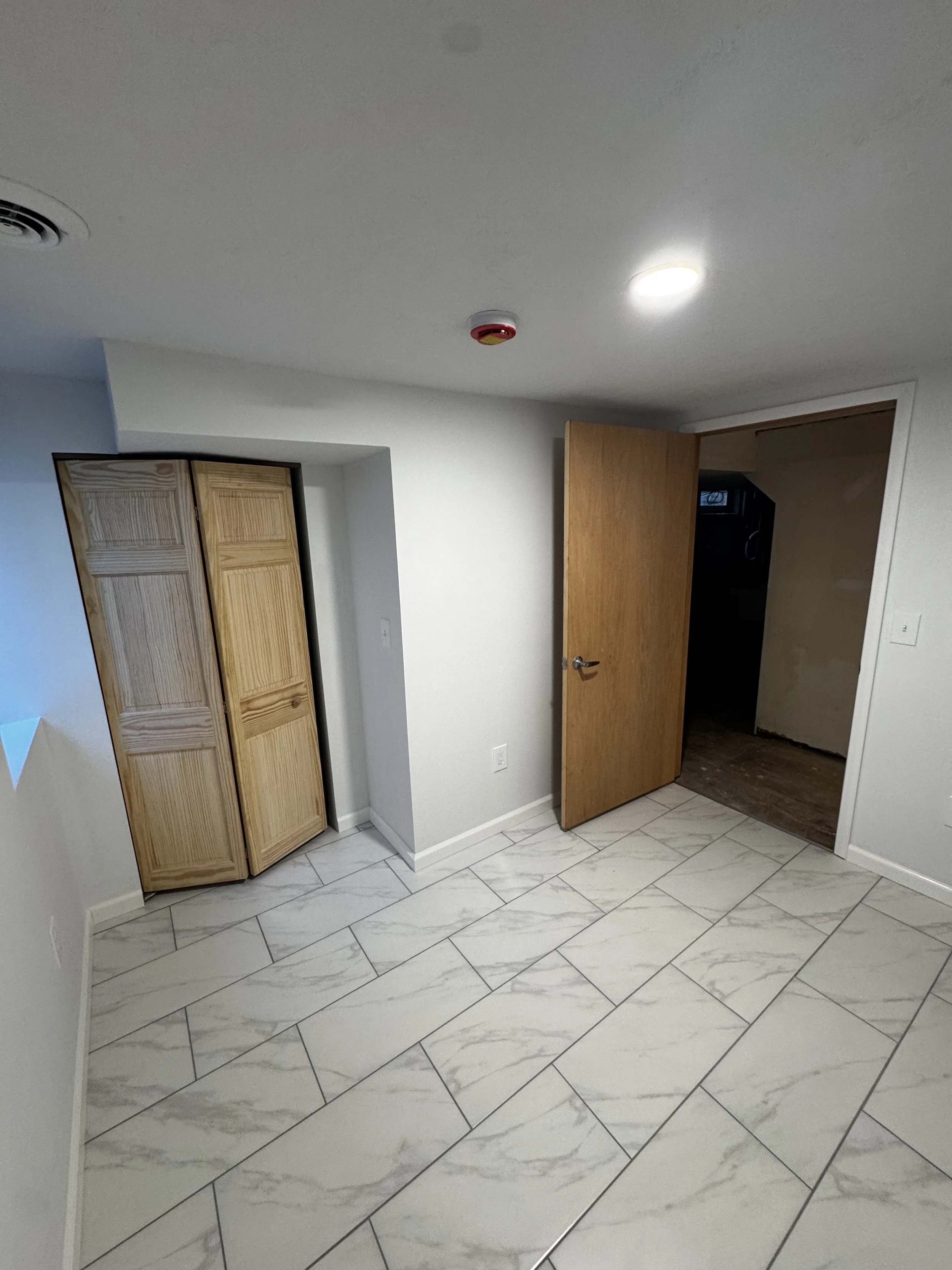 Empty room with white walls, marble tile floor, open wooden door, and small closet with beadboard doors.