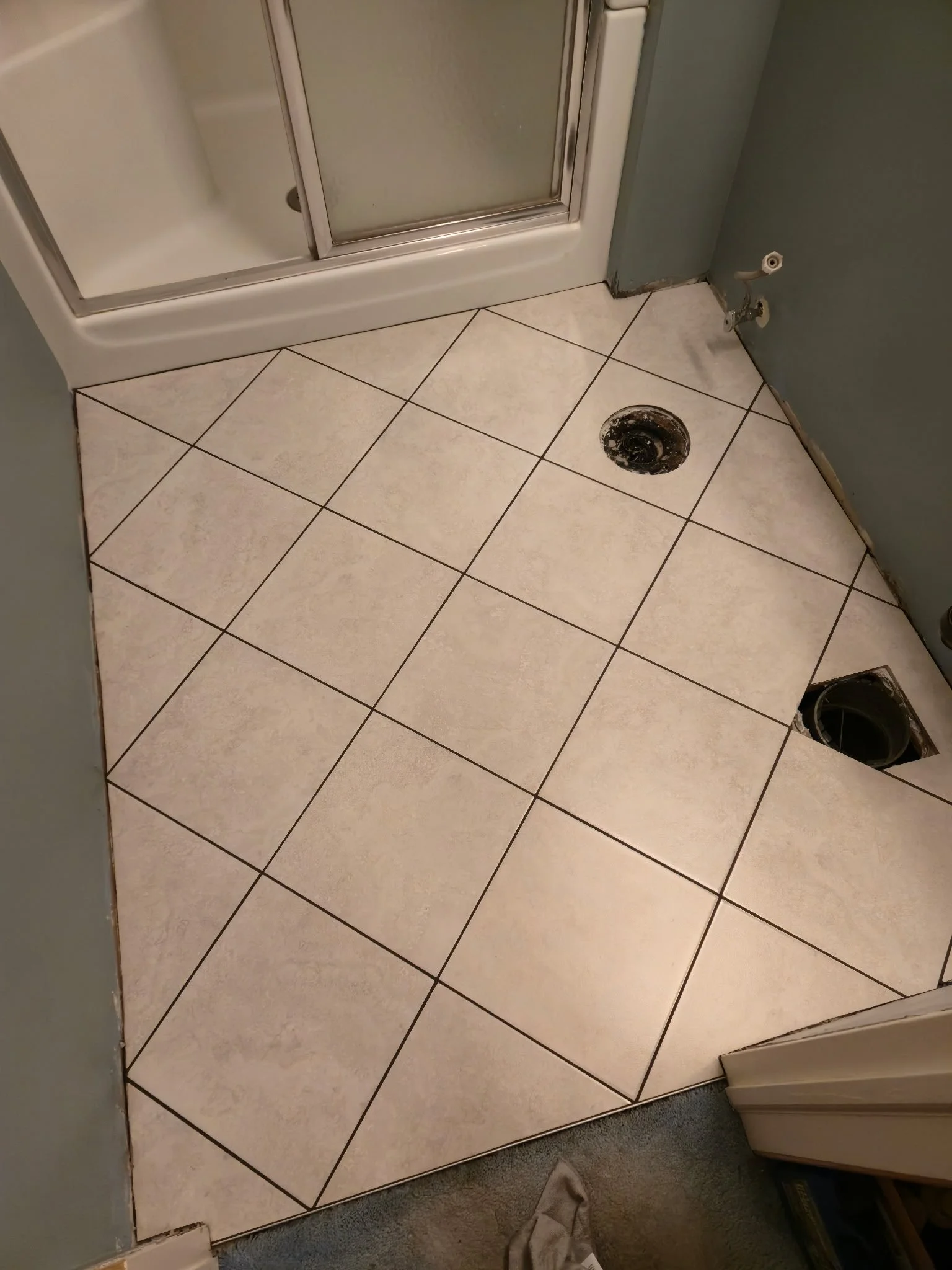 Bathroom with a partially removed tile floor, two open drain openings, and a shower stall in the upper left corner.