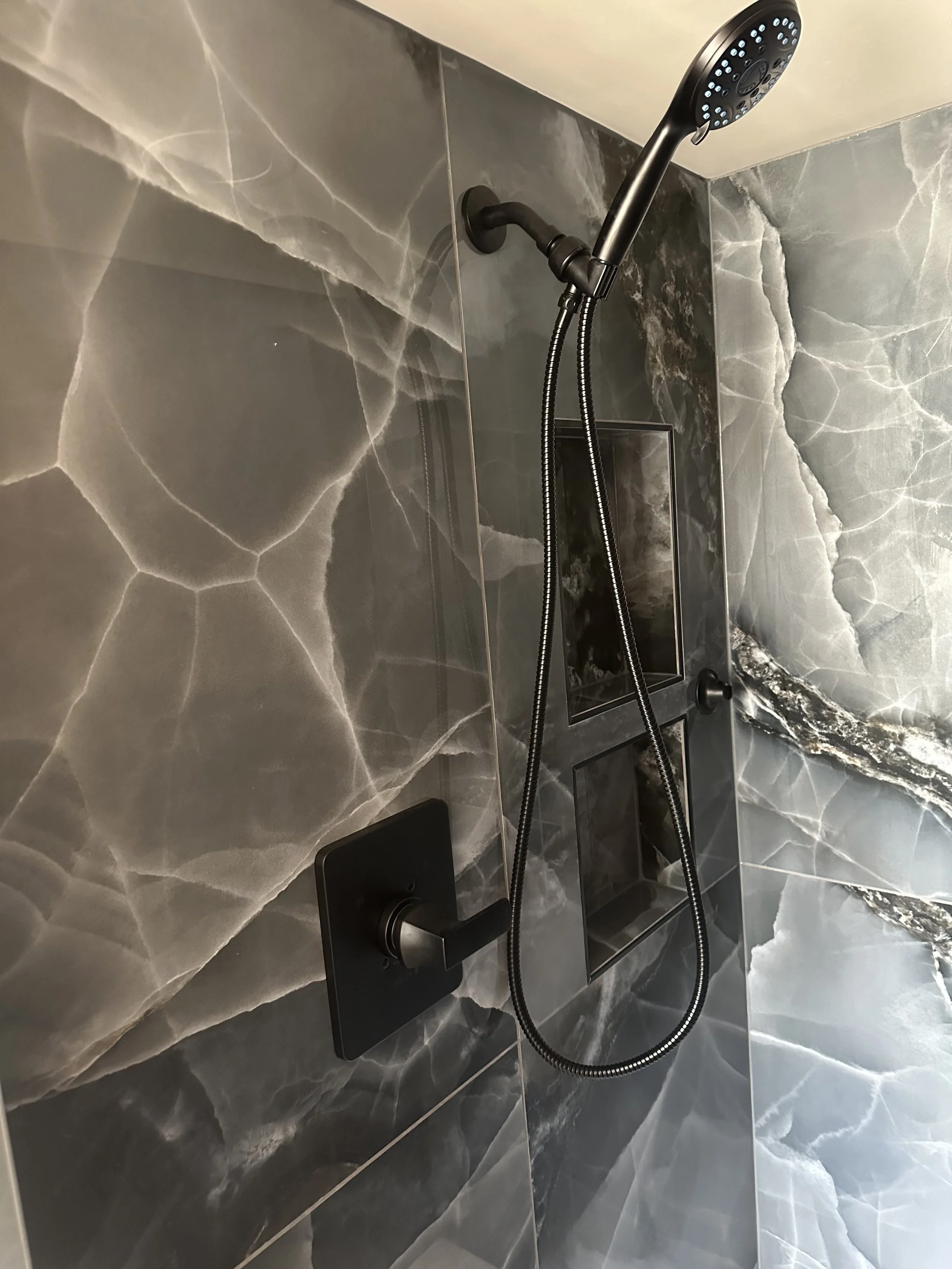 Marble-patterned shower with black fixtures and a handheld showerhead.