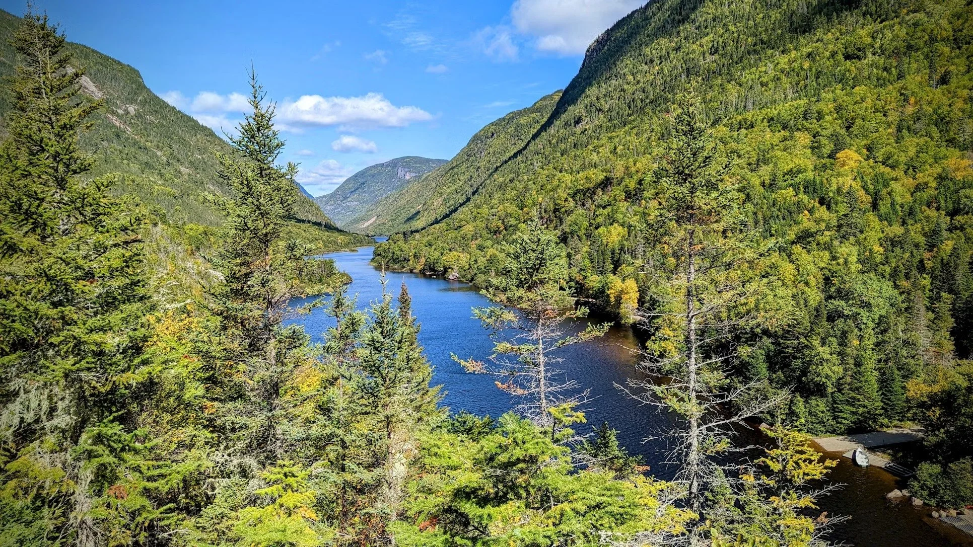 Paysage avec une rivière entourée de forêts et de montagnes verdoyantes sous un ciel bleu.