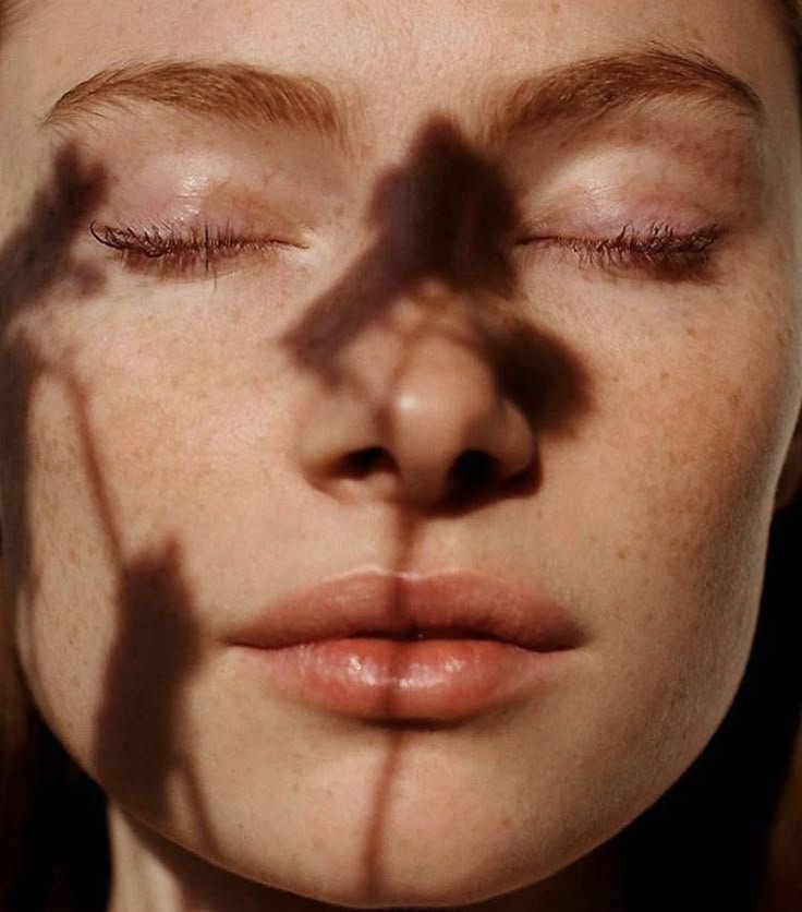 Close-up of a person's face with eyes closed, shadows from a plant cast across their face creating patterns.