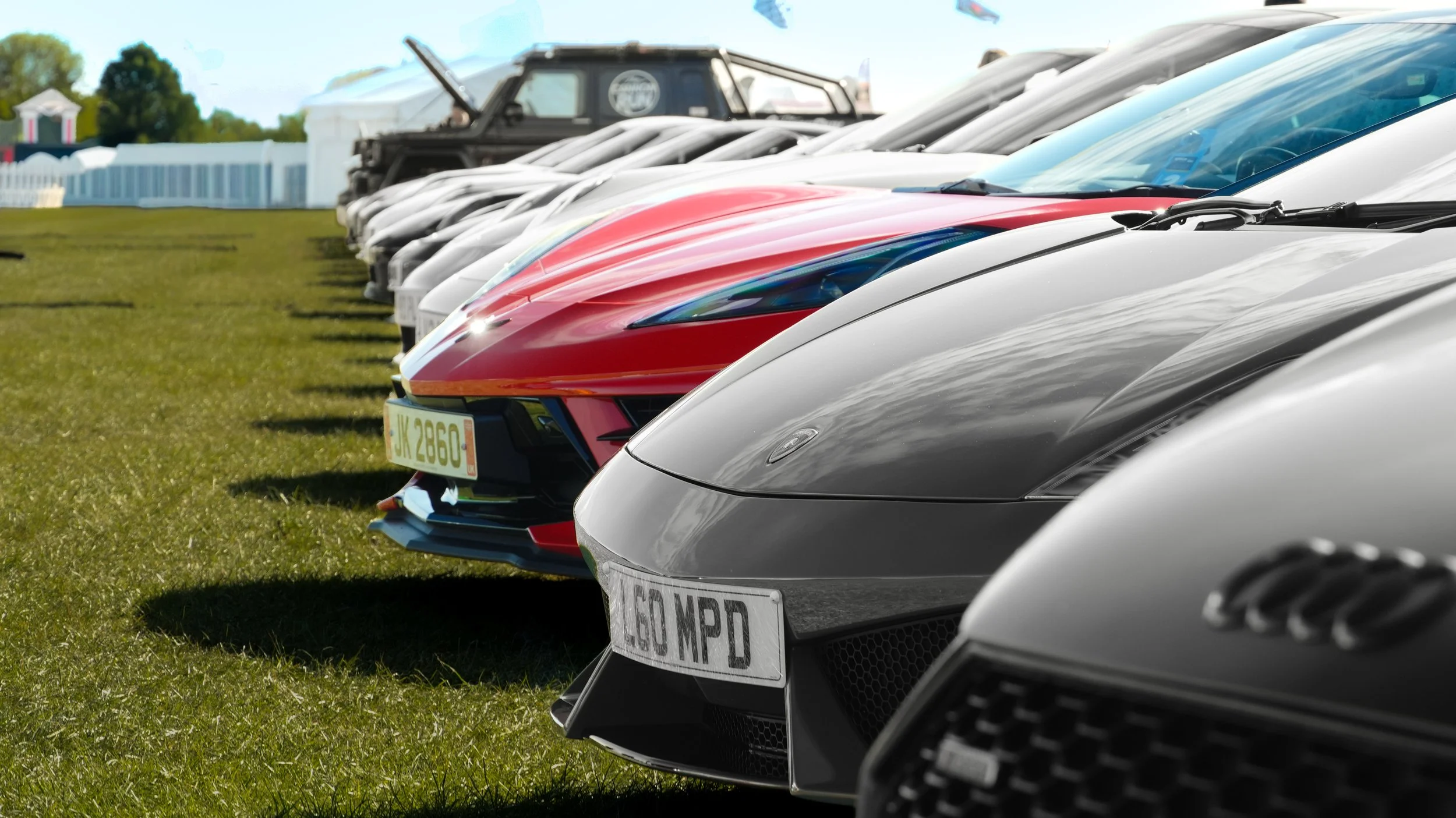 Lineup of various sports cars and an off-road vehicle parked on grass at an outdoor event.