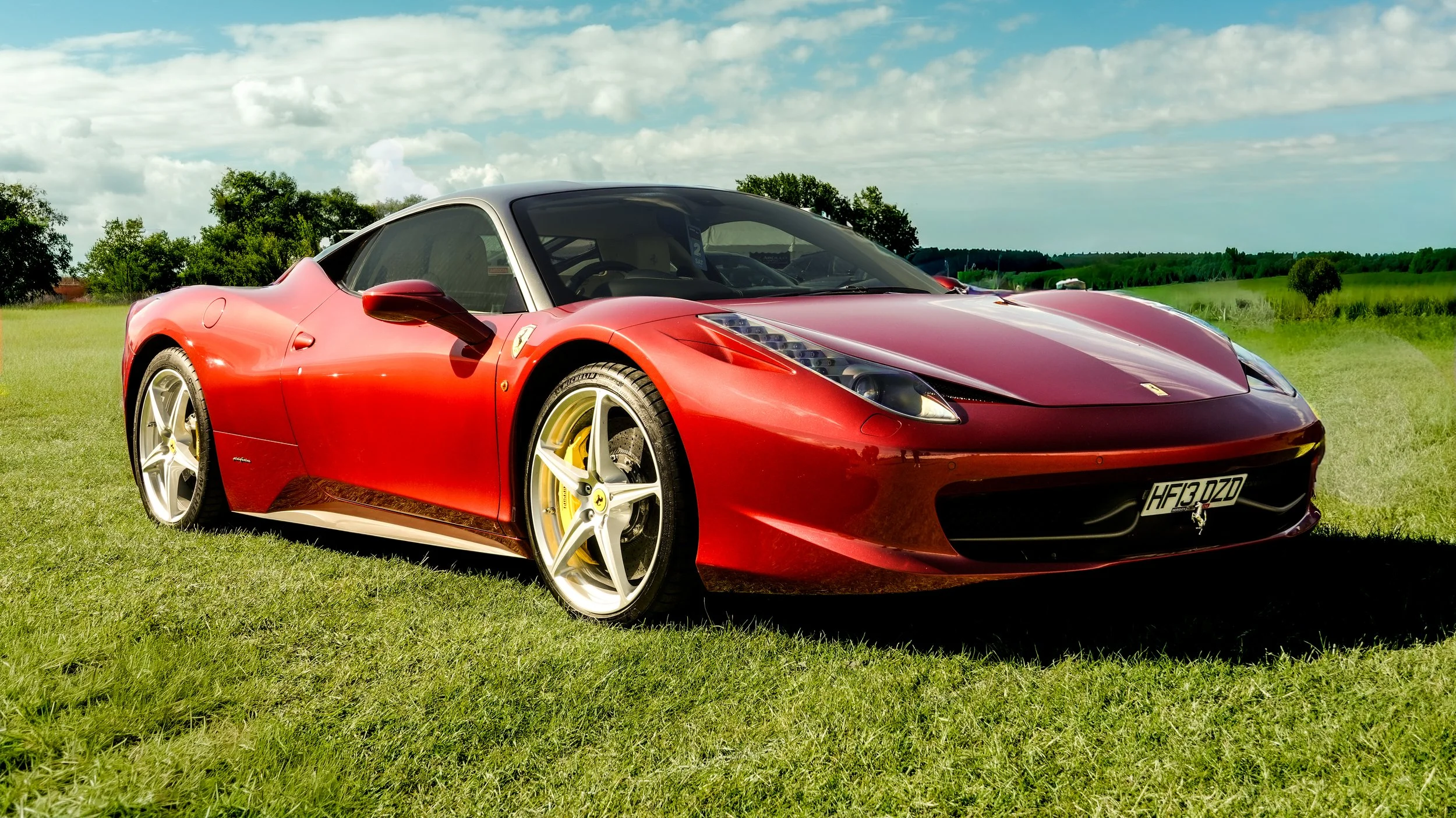 Red Ferrari sports car parked on green grass field under cloudy sky.