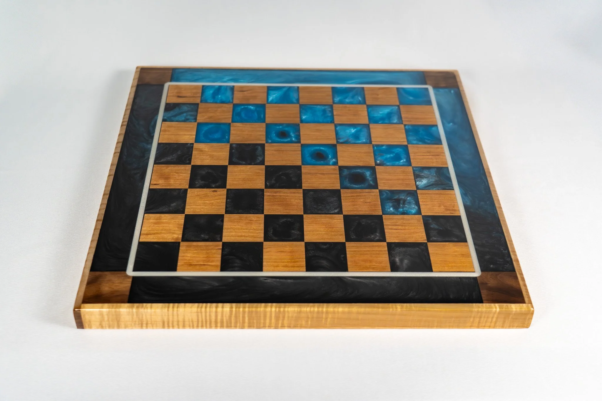 A chessboard with a wooden frame and a border of blue and black marble-like inlay, set on a white surface.