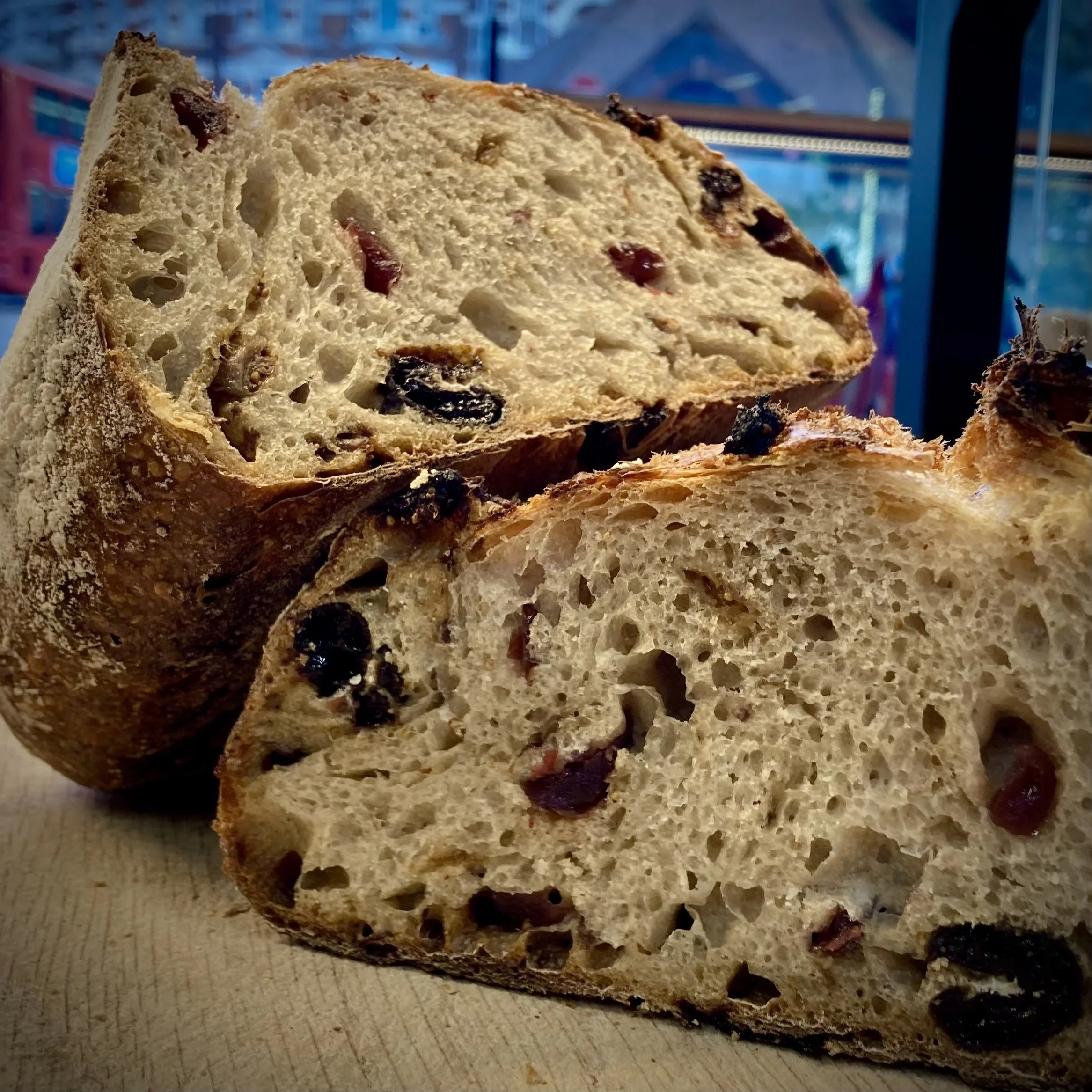 Sliced loaf of artisan bread with visible raisins and cranberries, showing a rustic crust and airy interior on a wooden surface.