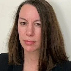 Portrait of a woman with shoulder-length brown hair, wearing a black top against a white background.