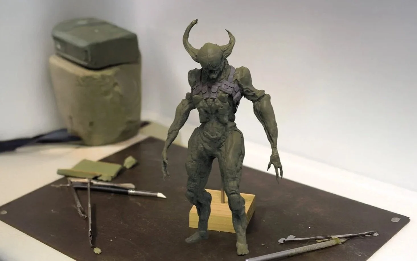 a photo of a sculpture made in clay, of a creature design made by professional freelance concept artist miguel nogueira, the clay is green, and there are a few sculpting tools featured on the table