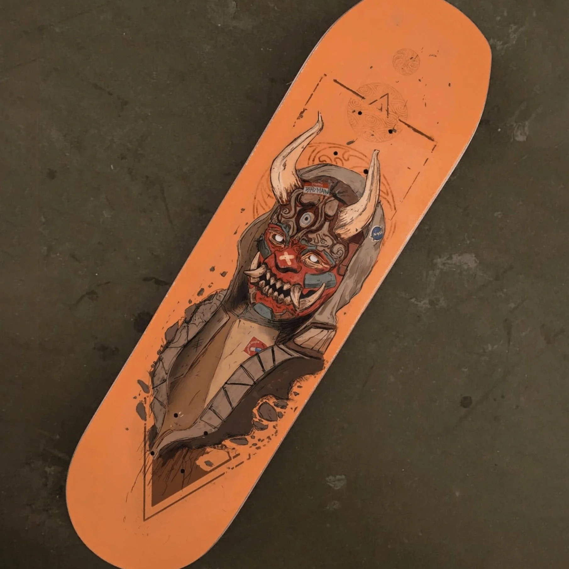 A skateboard deck featuring an illustration of a fierce, horned demon with sharp teeth, red face, and multiple eyes, set against an orange background.