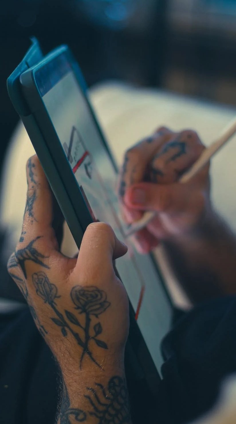 Close-up of a person with tattoos on their hand using a smartphone and stylus.