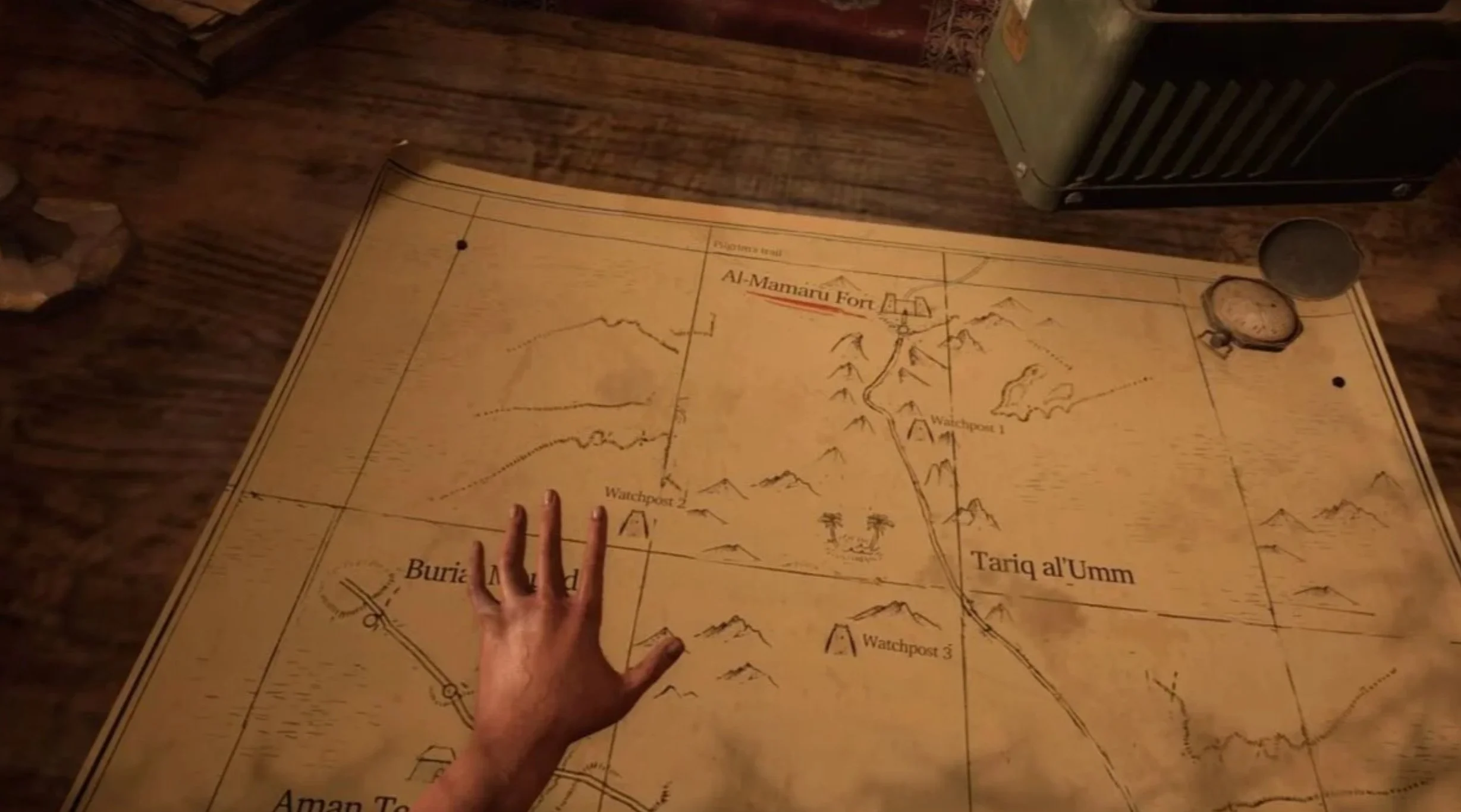 A person’s hand pointing to a map that shows the Al-Mamunu Fort and surrounding landmarks, laid out on a wooden table.