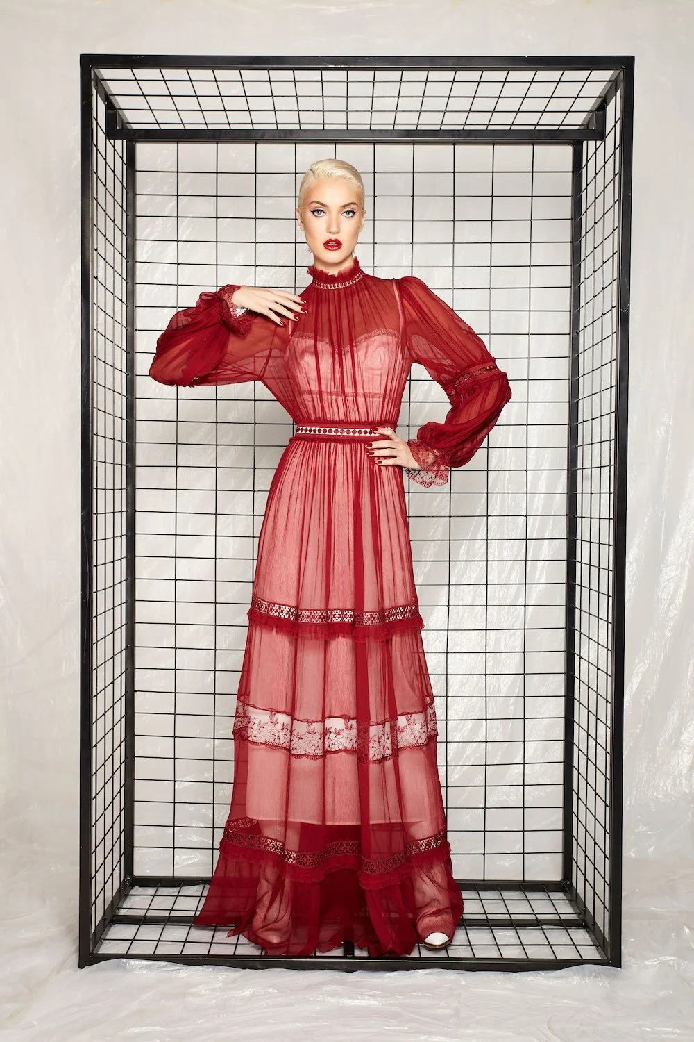 A woman in a sheer red dress with lace details stands inside a black wireframe cube.