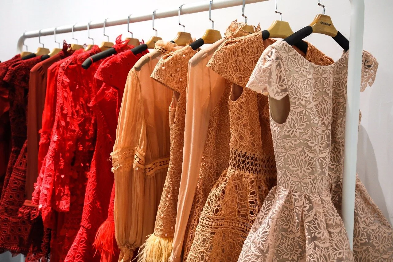 A clothing rack with various dresses in shades of red, orange, and beige, featuring lace and embroidered designs.