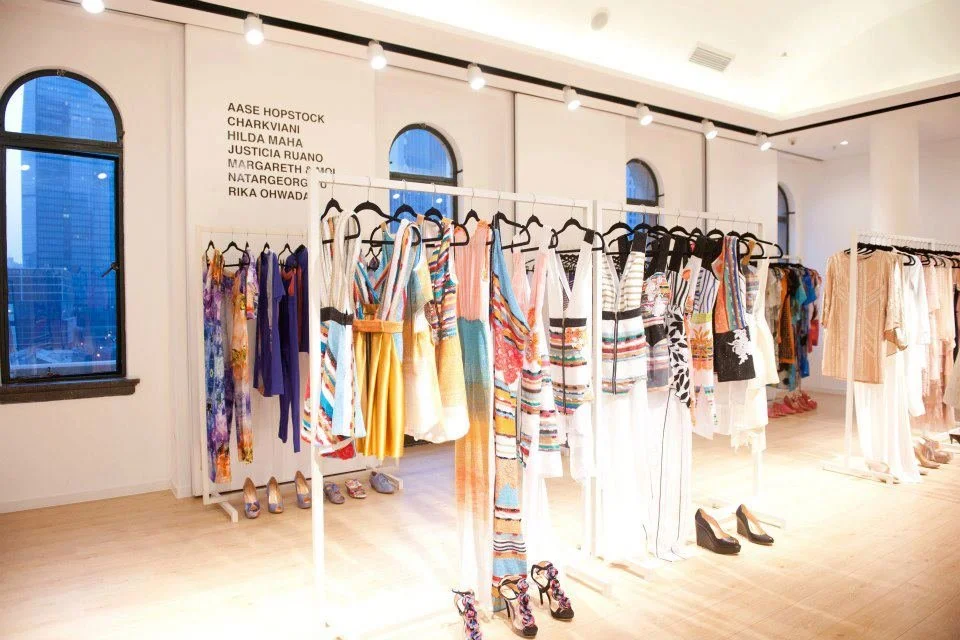 Clothing racks with colorful dresses and skirts in a boutique store, with shoes displayed underneath.