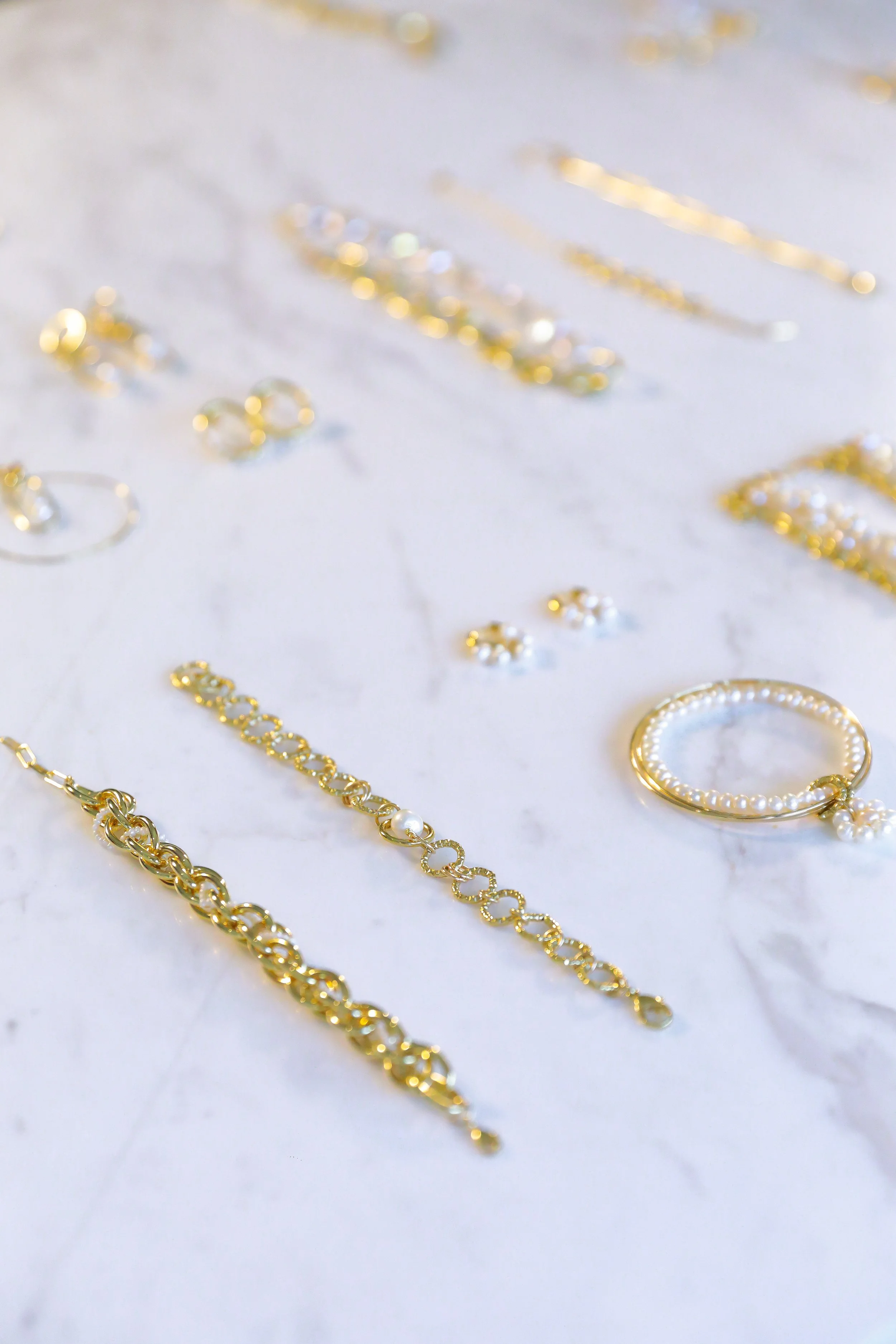 Gold jewelry including bracelets, earrings, and rings with pearl accents laid out on a white surface.
