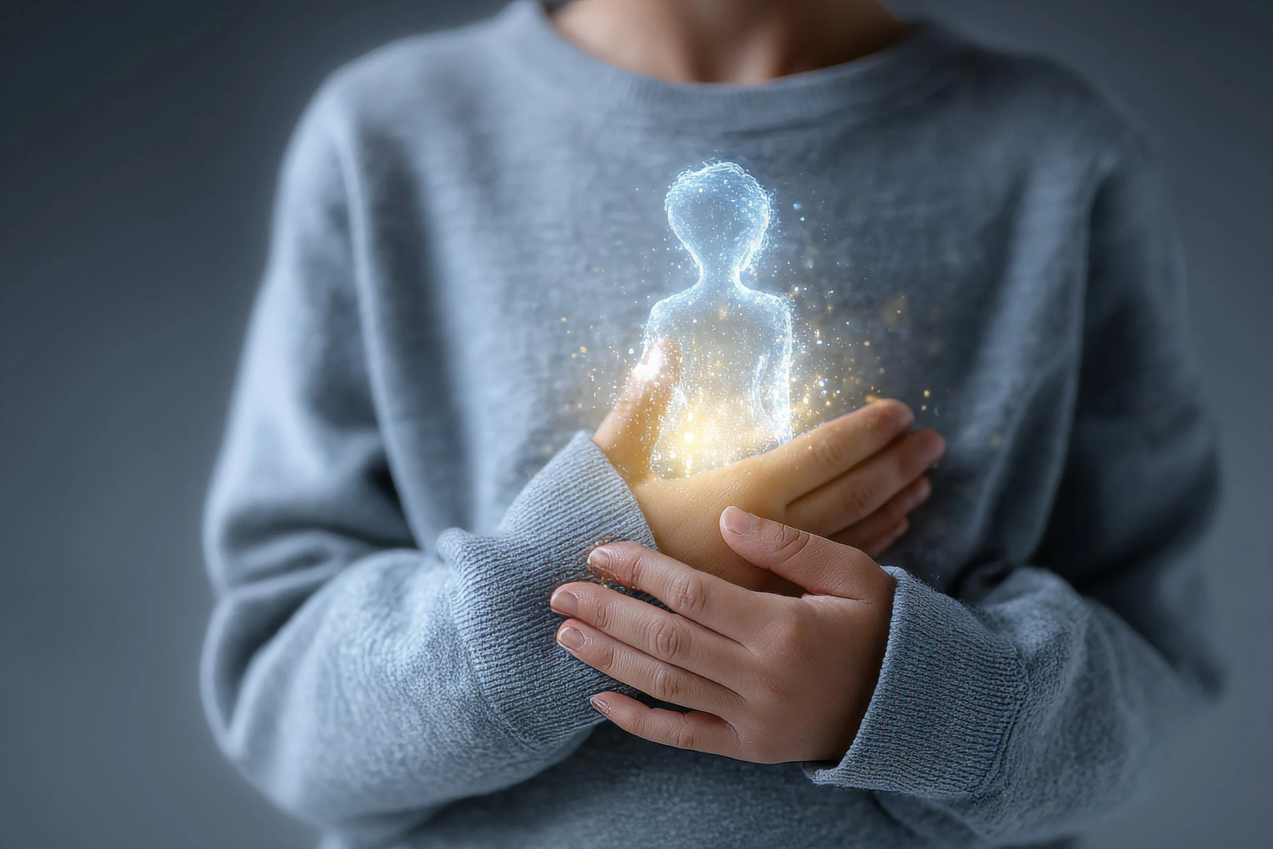 Child in grey sweatshirt holding their chest with a holographic, glowing silhouette of a person emitting sparkles, representing inner child healing