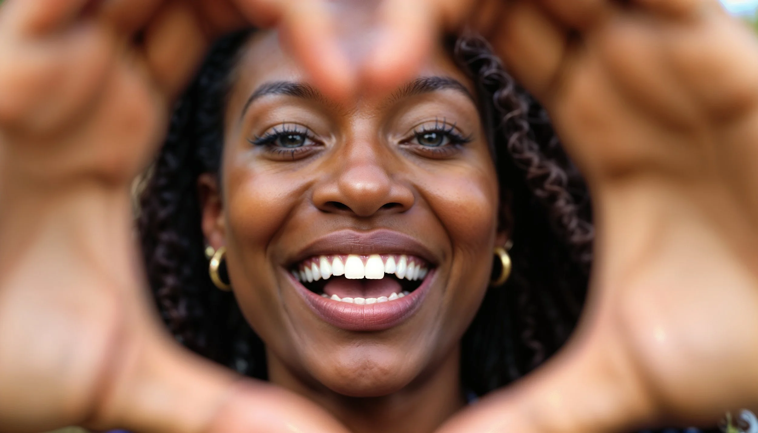 A beautiful black woman smiling, with her face framed with her hands making a heart shape to represent that she loves herself