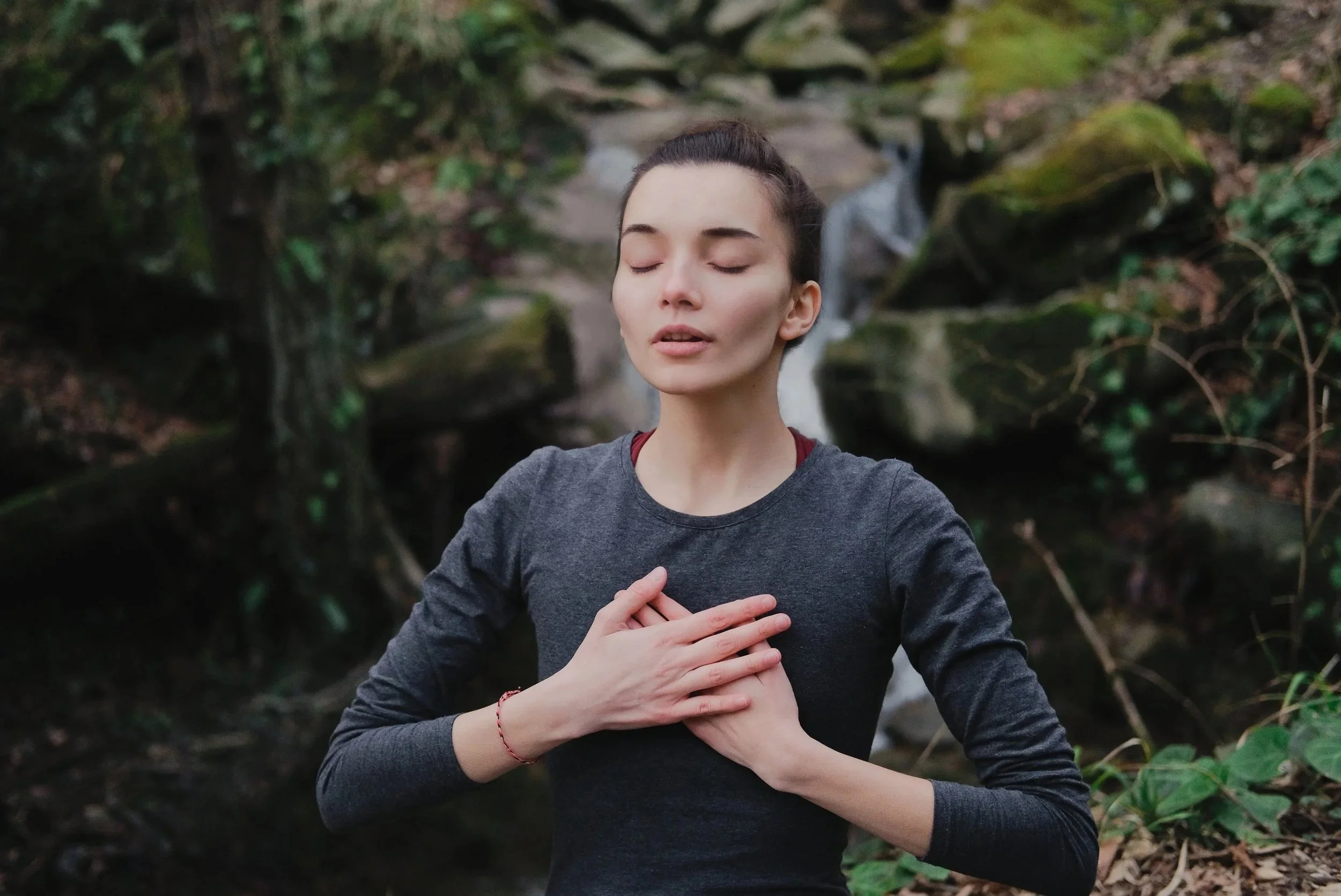 Beautiful young woman with her hands on her heart in a natural setting, illustrating a deep inner connection and self love