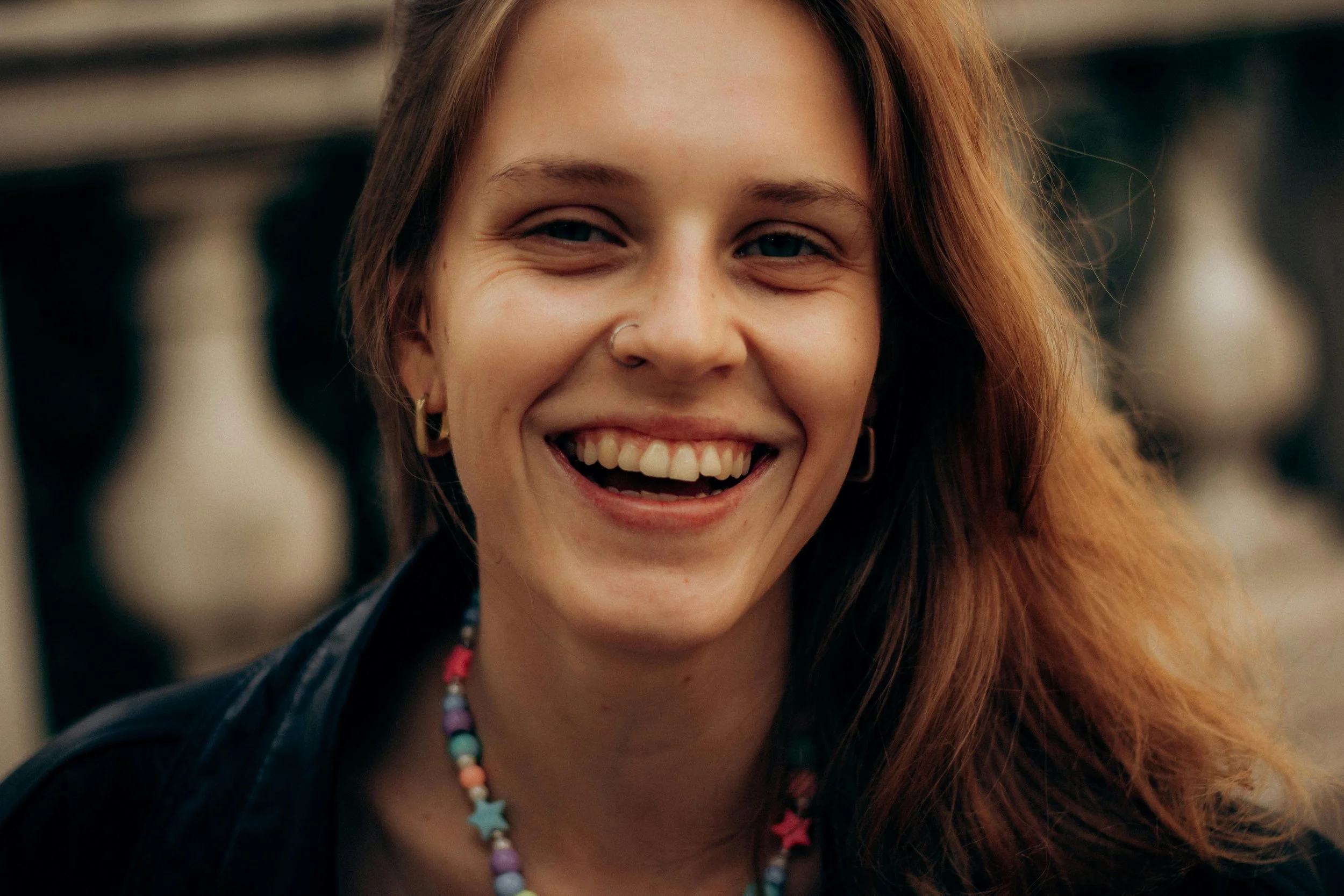 A happily smiling woman, wearing big earrings and a colourful, simple beaded necklace.