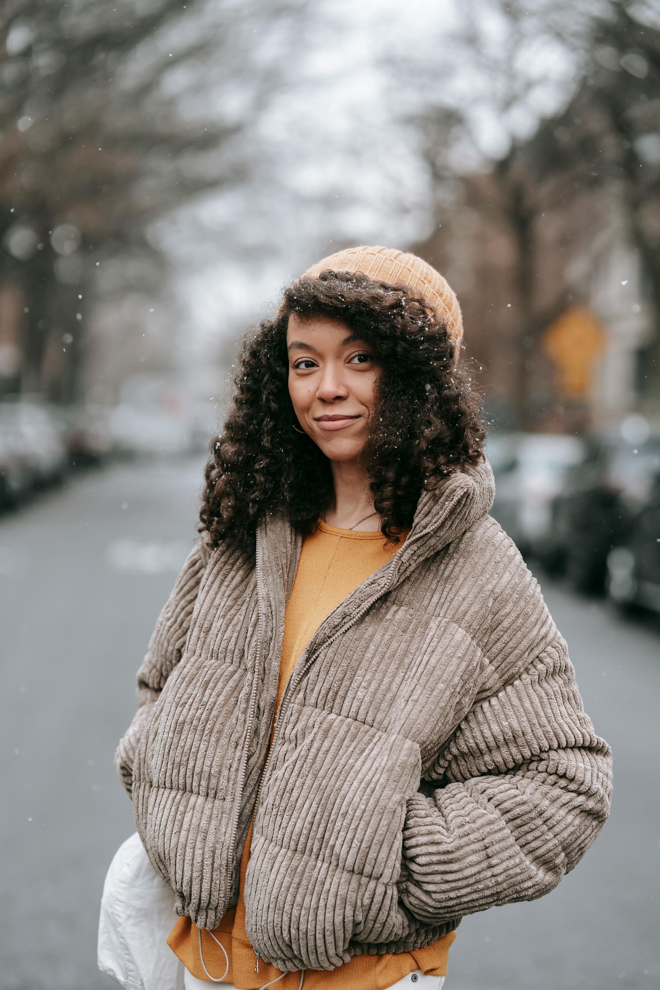 A brightly smiling Black woman with long, curly hair, wearing a comfortable winter coat.
