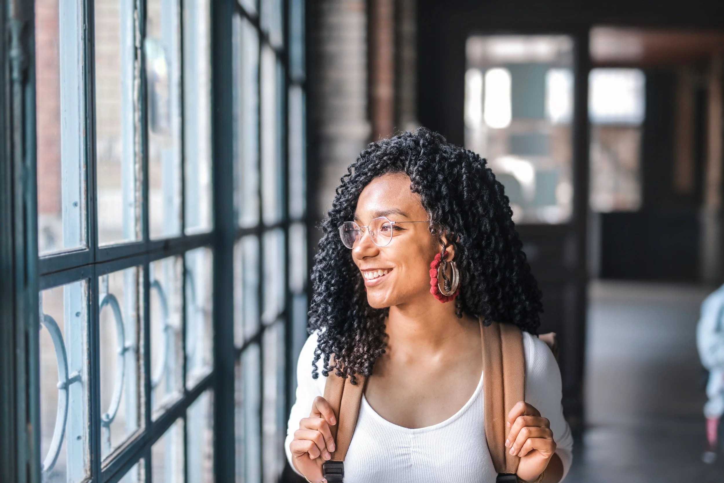 A smiling person looking out of a window, pausing thoughtfully