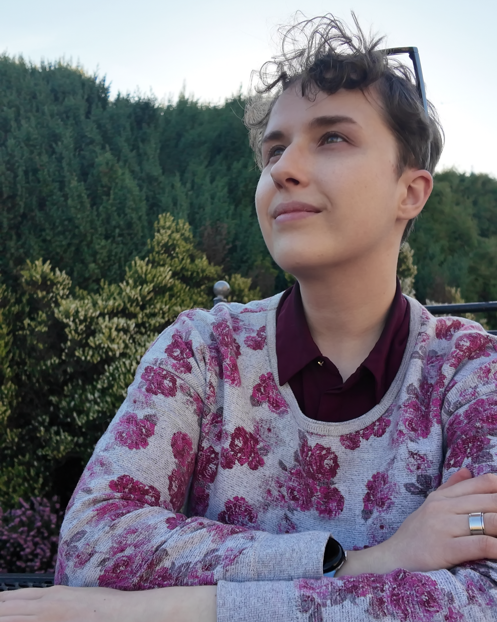 Max, wearing a purple shirt with a cardigan on top with purple flowers, looking up at the sky, smiling.