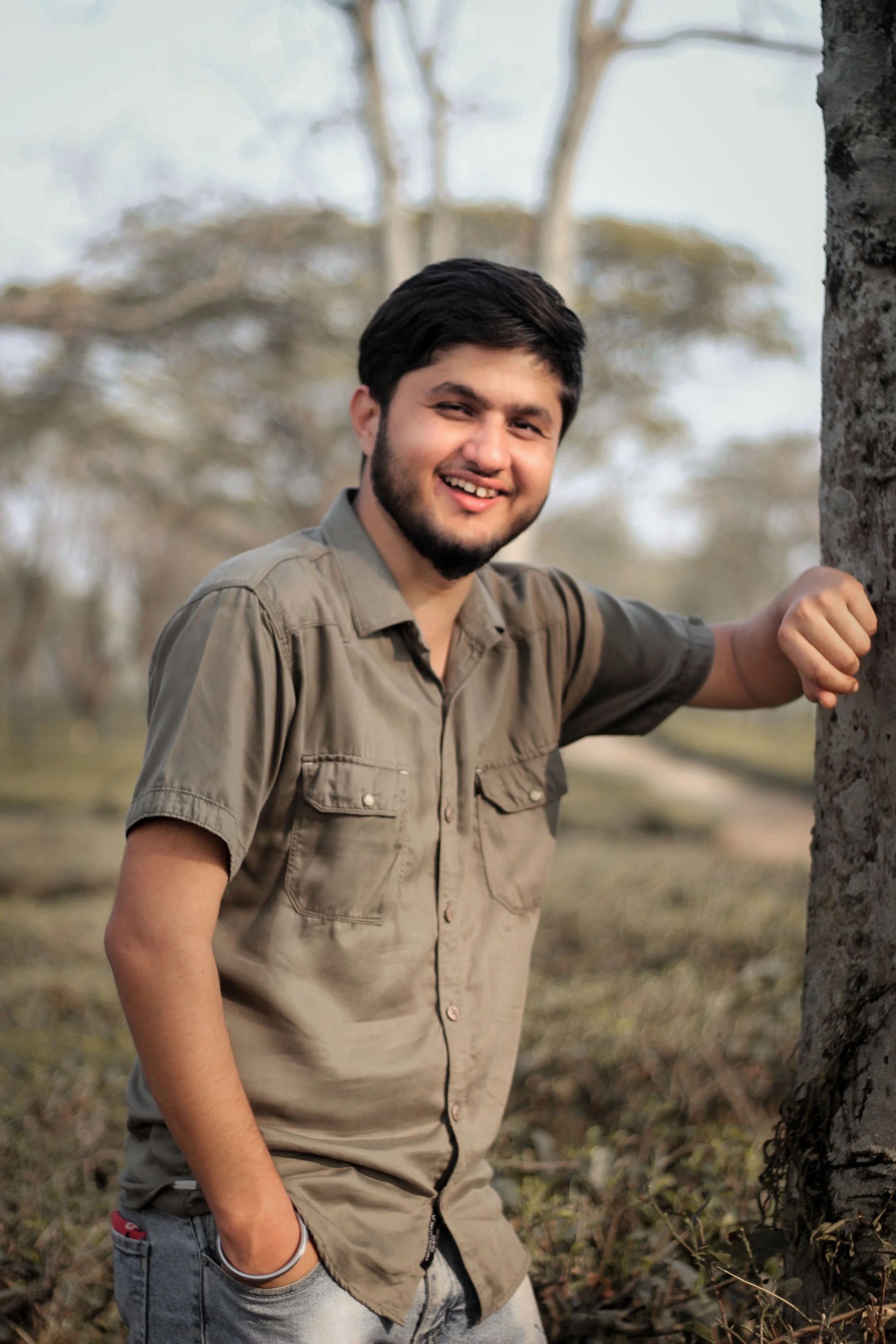 A smiling man leaning against a tree