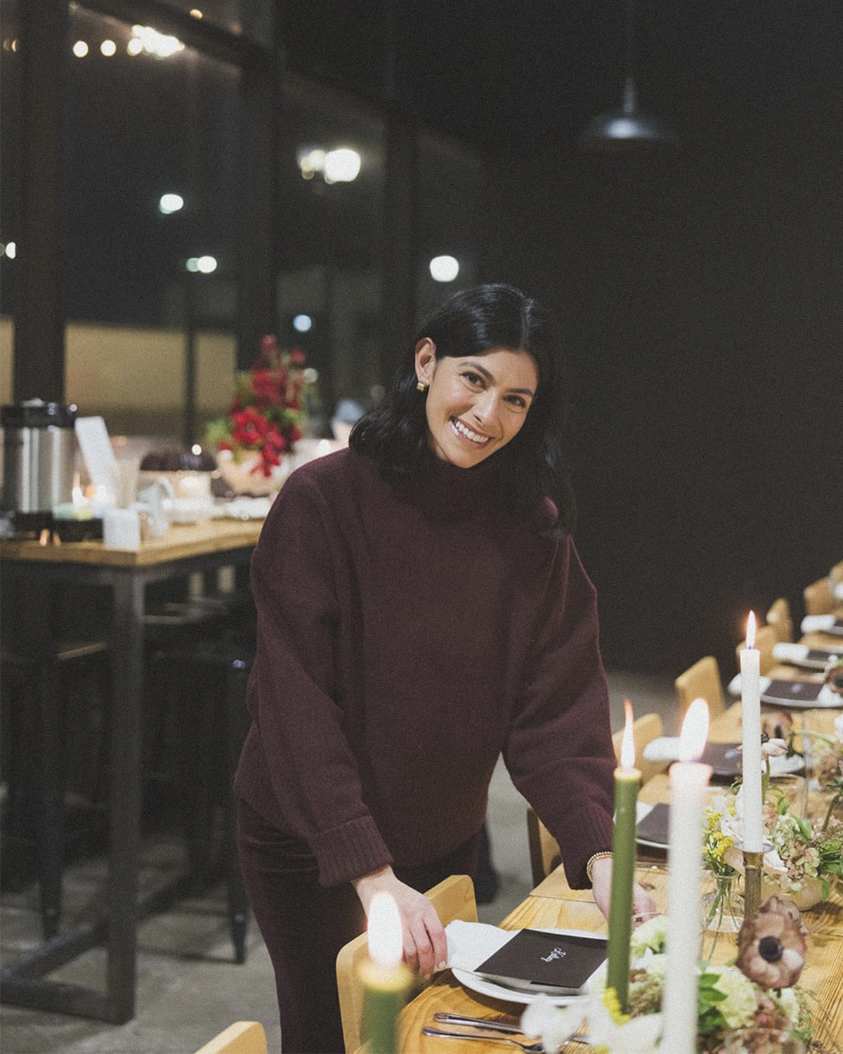 Sophia Gordon with black hair smiling and standing at a decorated dining table indoors at night.