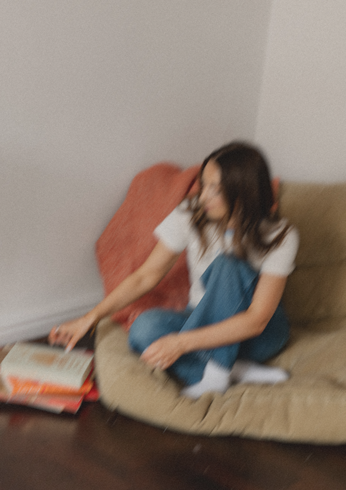 Emily Rose sitting on a beige couch, reading a book and looking at her phone.