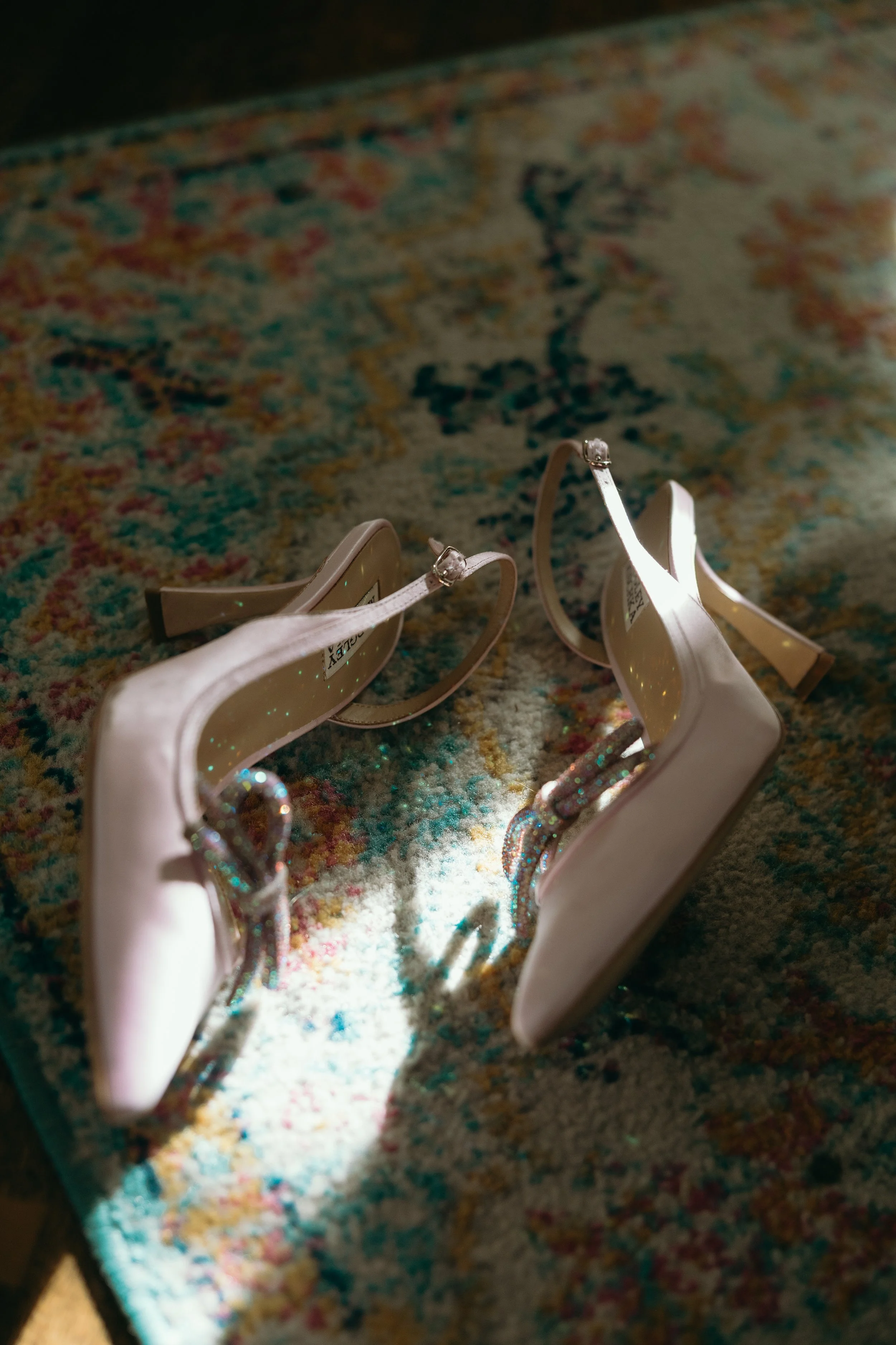 A pair of pink high heel shoes with glittery straps resting on a colorful patterned rug.