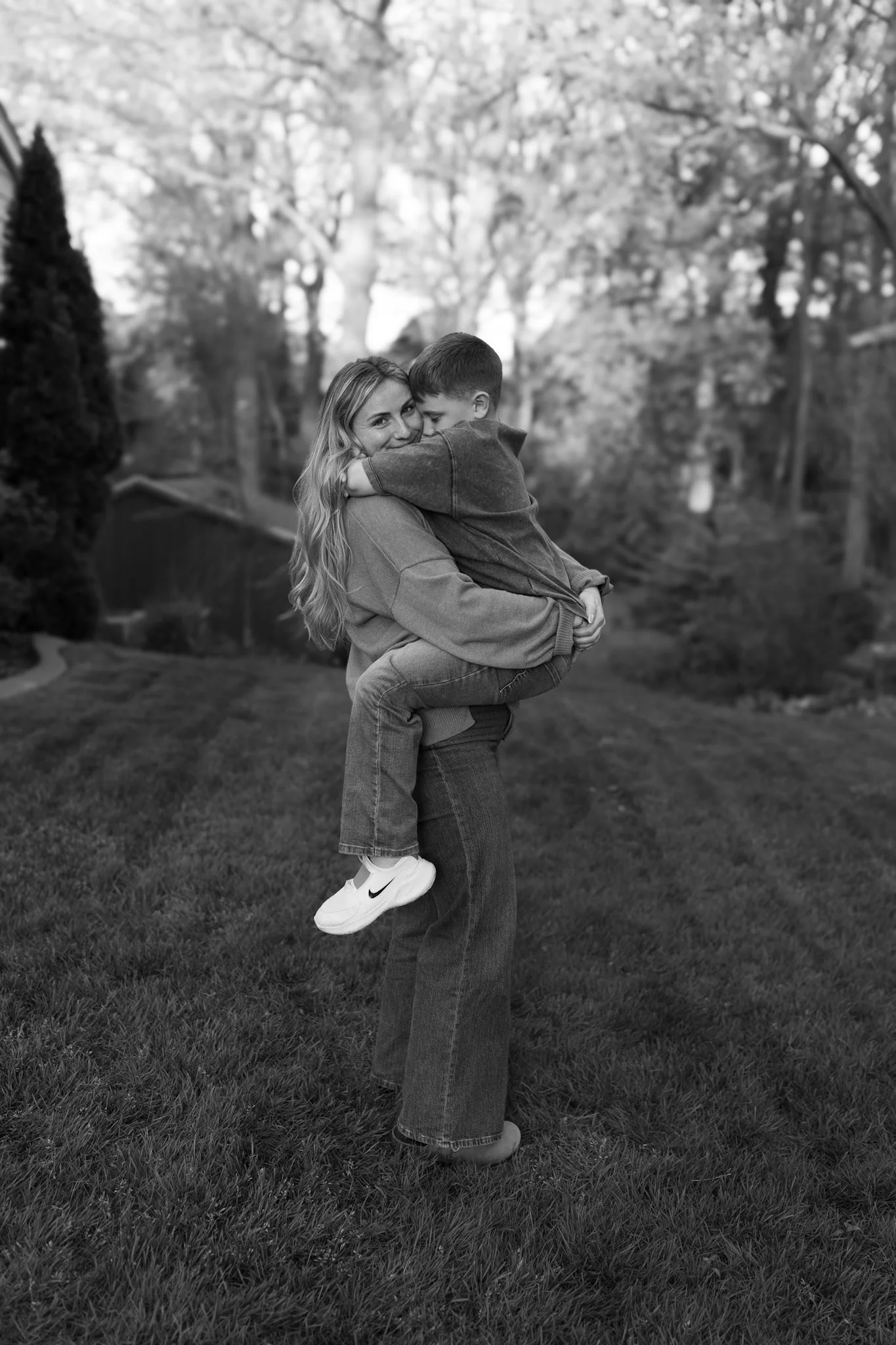 A woman giving a piggyback ride to a boy in a park with trees and grass.