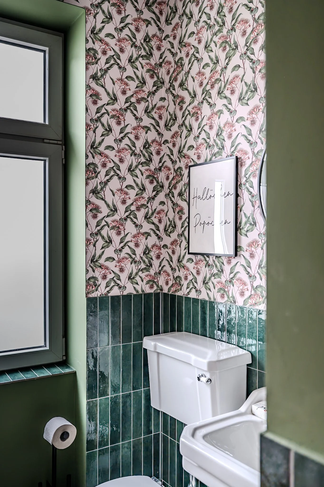 Badezimmer mit grünem Raufasertapete, einer kleinen Fenster, grünen Fliesen an der Wand, einem weißen Toilettenbecken und einer Wanddekoration mit italienischem Text.