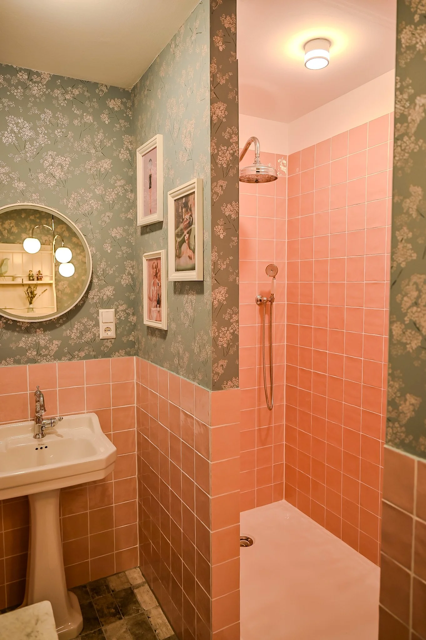 Ein Badezimmer mit lila Fliesen im Duschangebiet, einem weißen Waschbecken, einer Wand mit Blumenmuster und Bilderrahmen