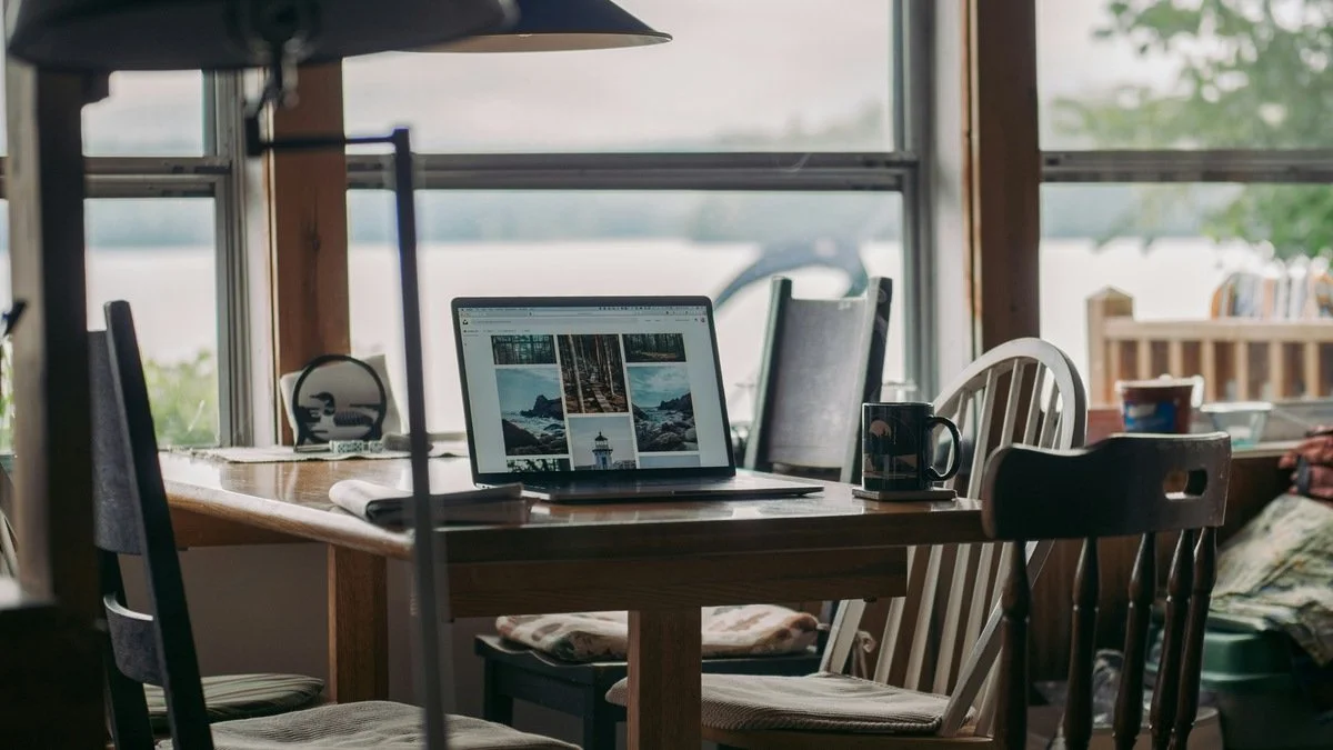 Laptop on wooden table with nature and water view through window — remote work and financial independence lifestyle.