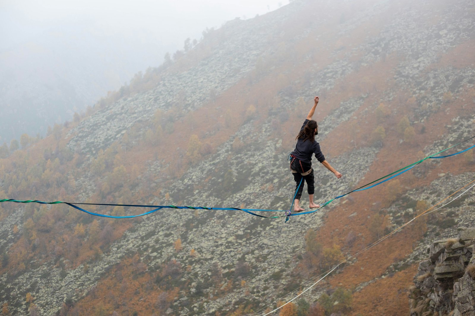Person walking a highline tightrope in mountains — representing the balance required to maintain a target portfolio allocation over time.