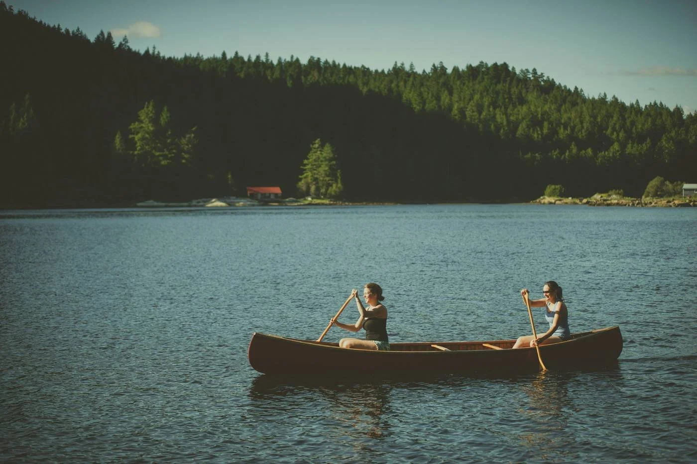 Two women canoeing on a calm lake surrounded by forest — active slow travel and mini-retirements on the path to FIRE.